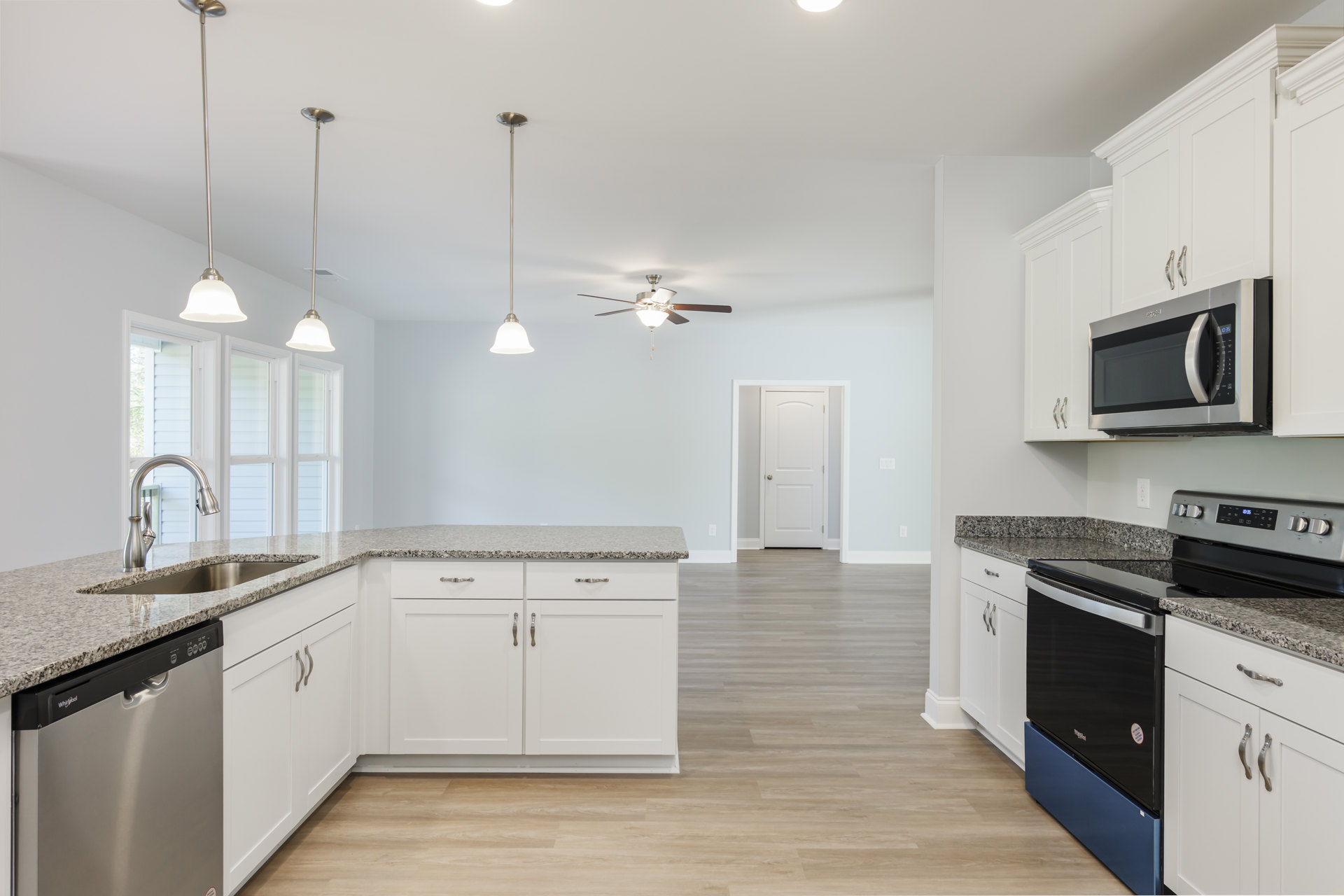 White kitchen cabinets with black appliances, open microwave door, wood flooring, white interior door, black television, silver pole with blue and yellow sign, stainless steel sink