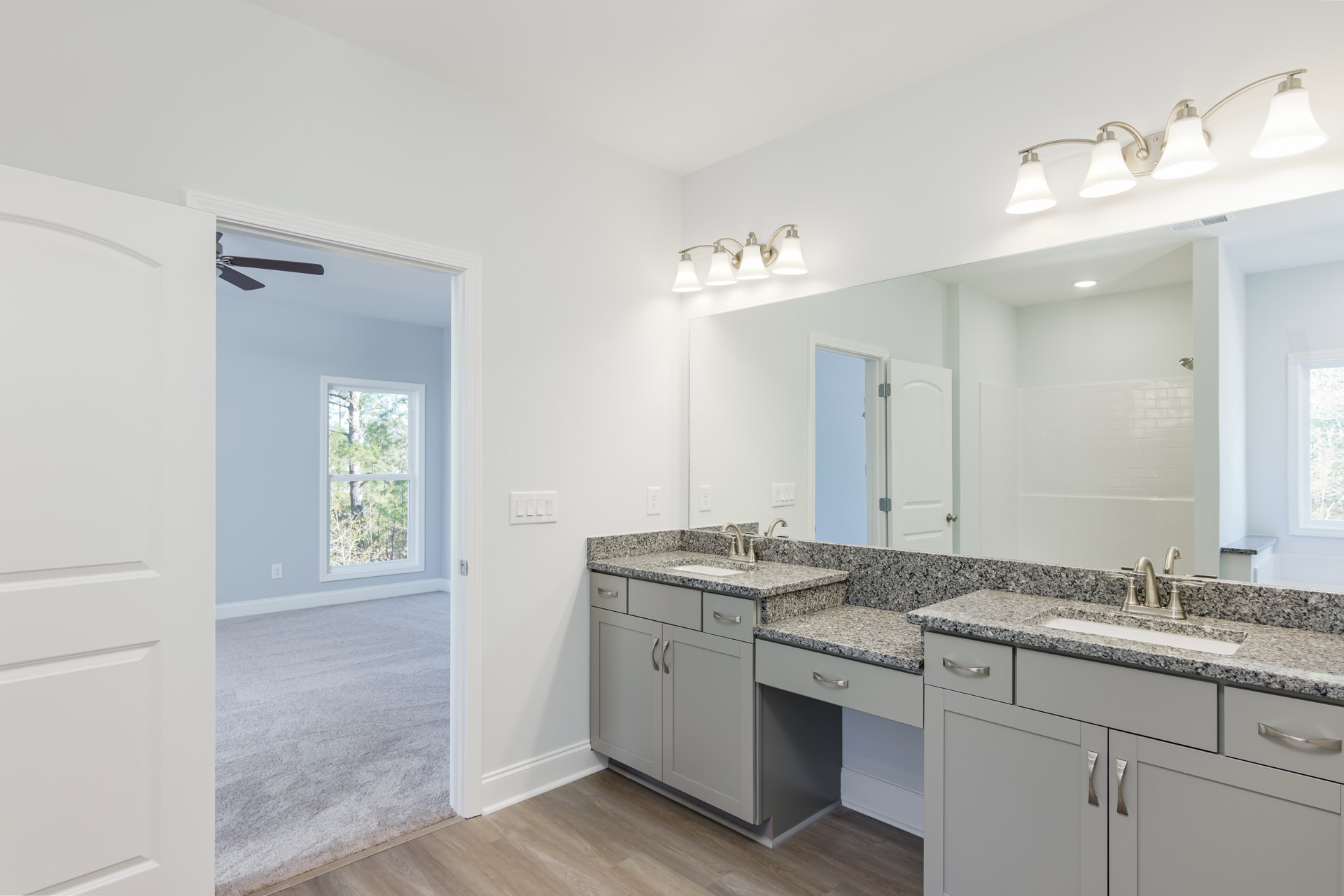 Bathroom with expansive mirror above dual sinks, white cabinetry, stone countertop, tile flooring, and window overlooking trees.