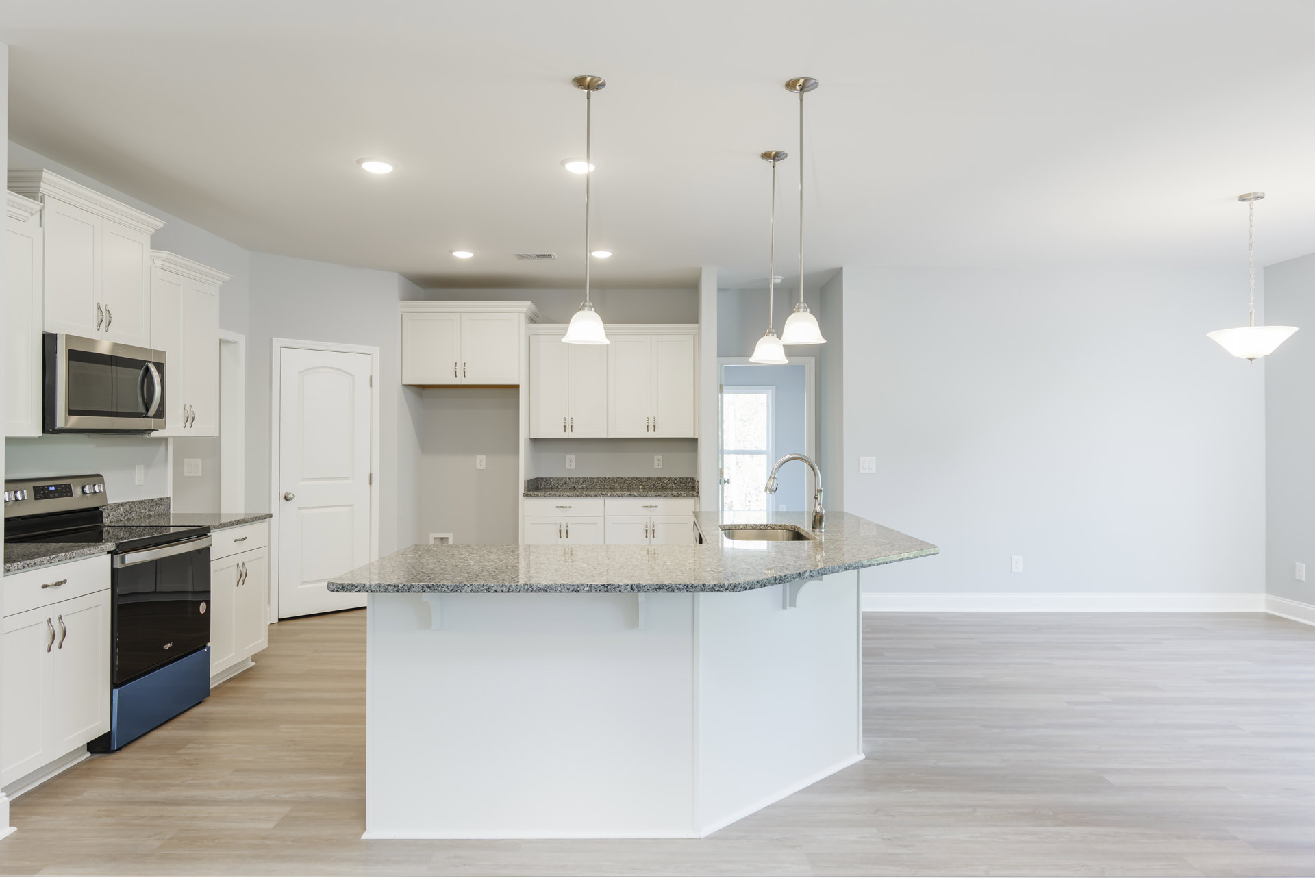 Granite kitchen island with white cabinetry, stainless steel microwave, pendant light on white pole, chain hanging from ceiling, white door with silver knob, and light wood