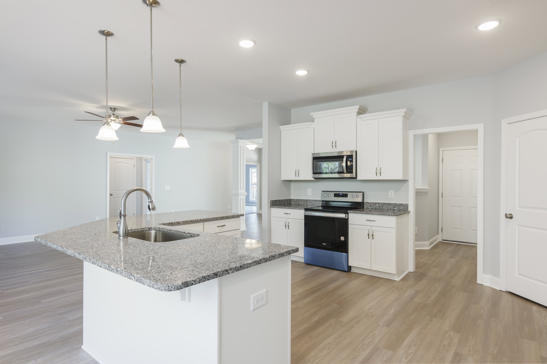 Granite countertops and white cabinets in a kitchen with a stainless steel microwave oven door open, sink set in the counter, stove with blue and silver handle, close-up of white