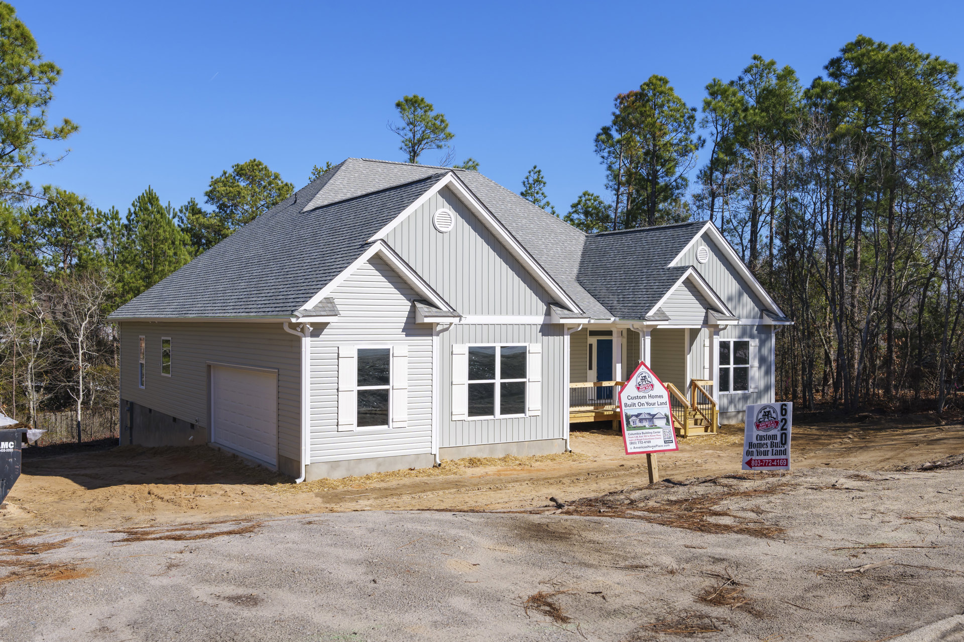 Two-story home with light siding, attached garage, large front windows, manicured lawn, and a wooden real estate sign near the driveway.