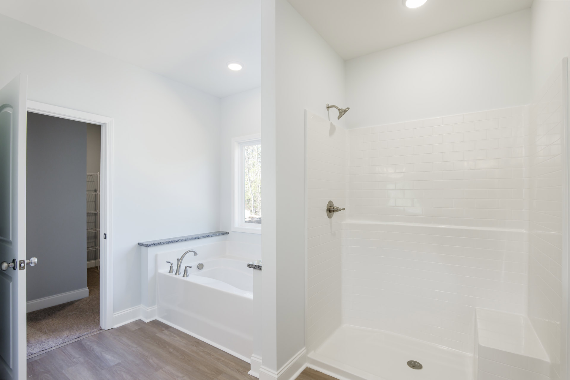 Bathroom with freestanding bathtub, glass-enclosed shower, white tile walls, wood flooring, and white trim