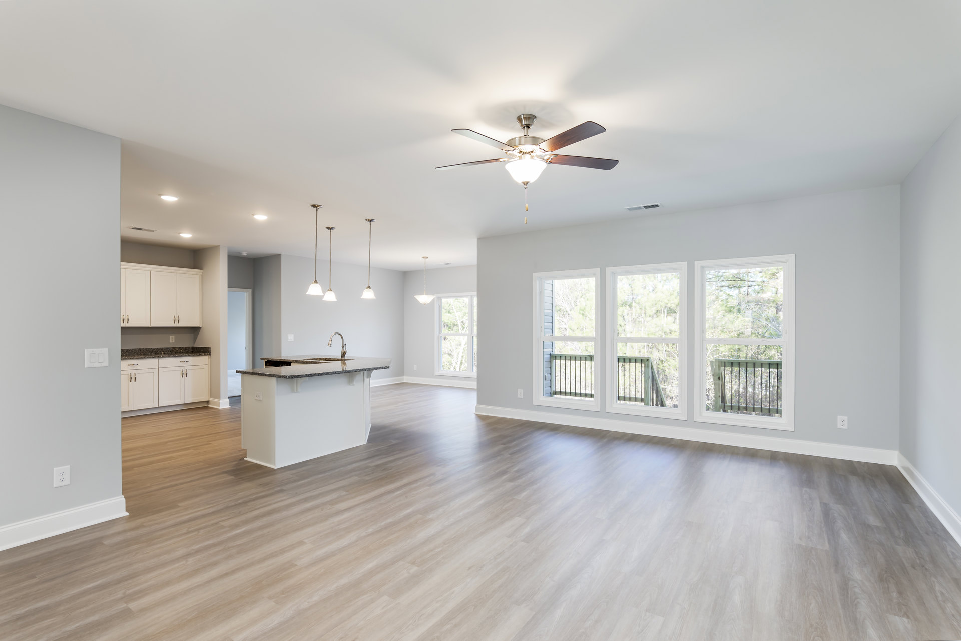 White kitchen island with built-in sink, hardwood flooring, ceiling fan with light, large windows overlooking trees and outdoor railing