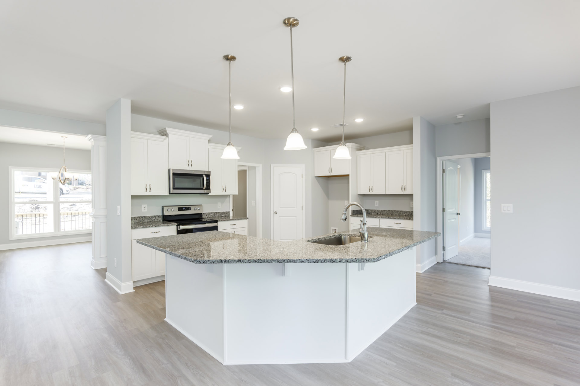 Marble kitchen island with waterfall edge, white cabinetry, stainless steel sink, tile backsplash, built-in microwave with white door, pendant lighting, and light wood flooring