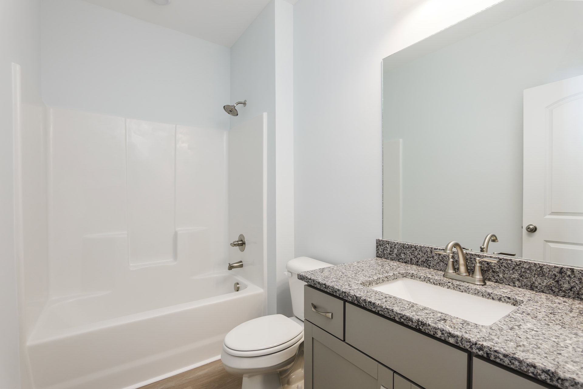 Modern bathroom featuring a white ceramic sink with chrome faucet, matching white toilet with lid closed, wall-mounted mirror above a light wood vanity, and a shower head against