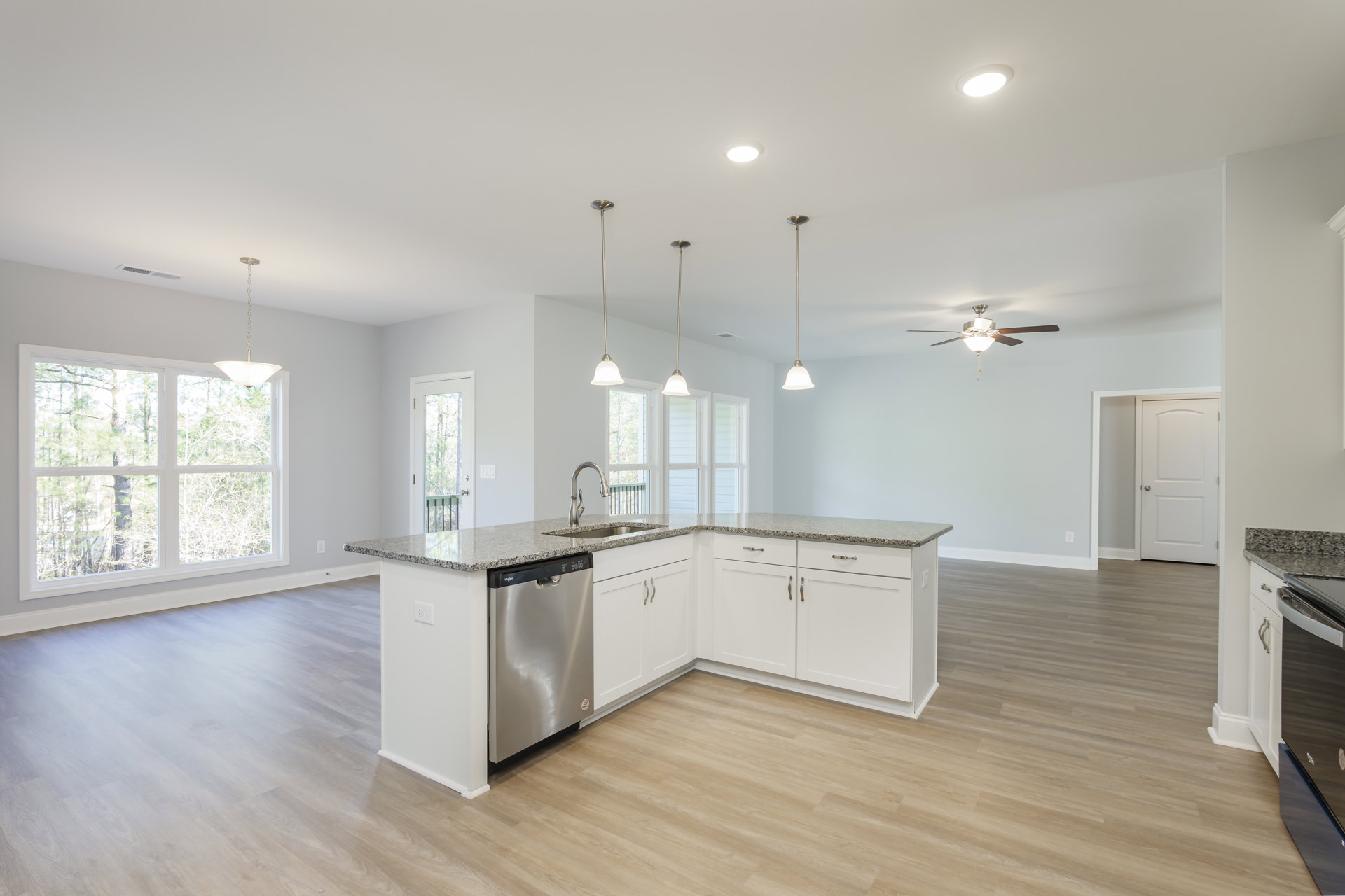 Modern kitchen with white cabinetry, stainless steel sink and dishwasher, stone countertop, ceiling light fixture, window overlooking trees, white door with silver knob, and