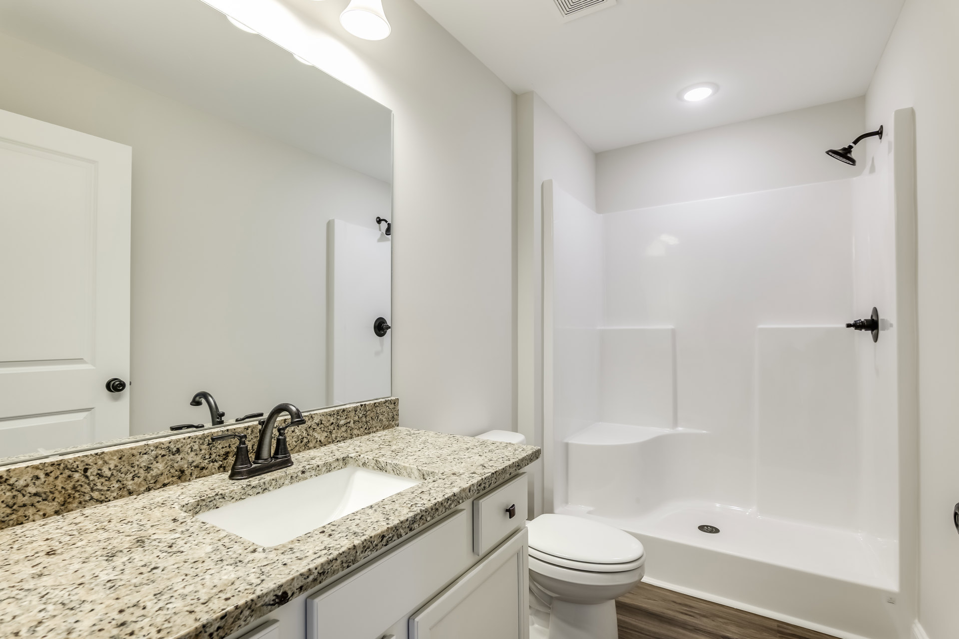 Bathroom featuring marbled bathtub with black tray, modern sink and faucet, white toilet, black shower head against tiled wall, large mirror reflecting indoor finishes.