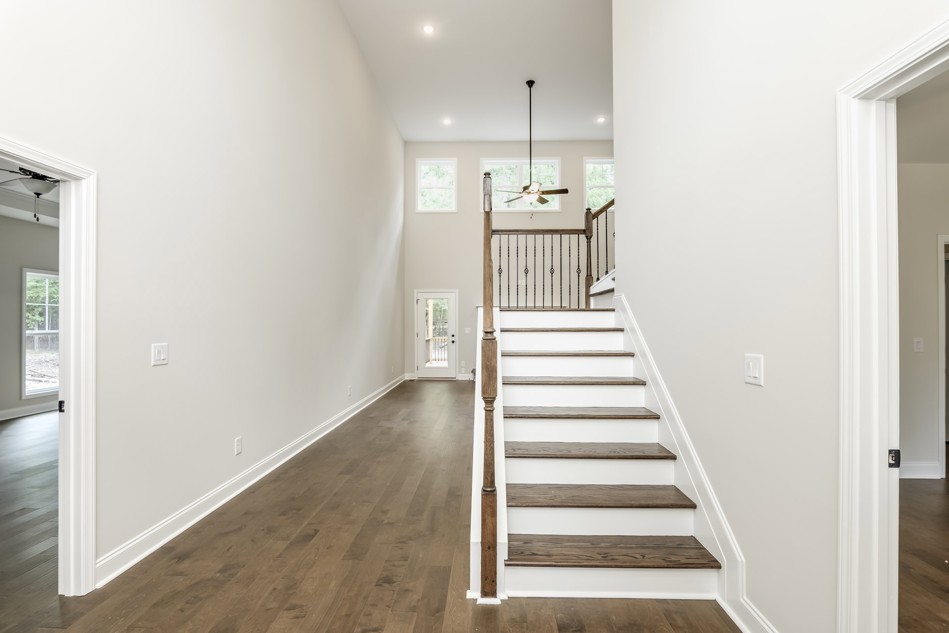 Wood staircase with matching railings, white plaster walls, laminate flooring, door with glass panels revealing trees outside, window with white frame, modern interior design
