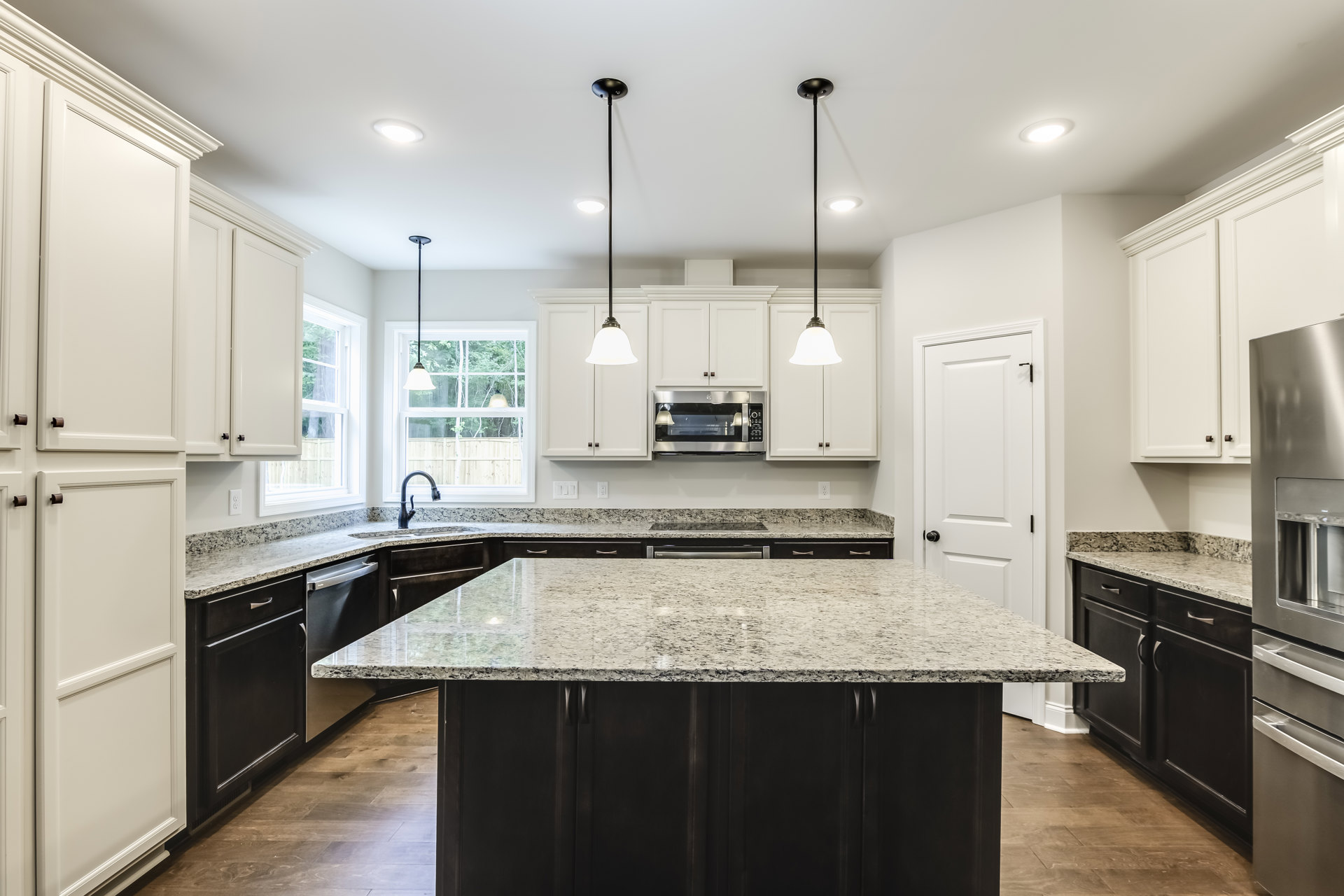 Granite countertops with black cabinetry, silver microwave with glass door, black faucet on marble surface, white wall, overhead lighting