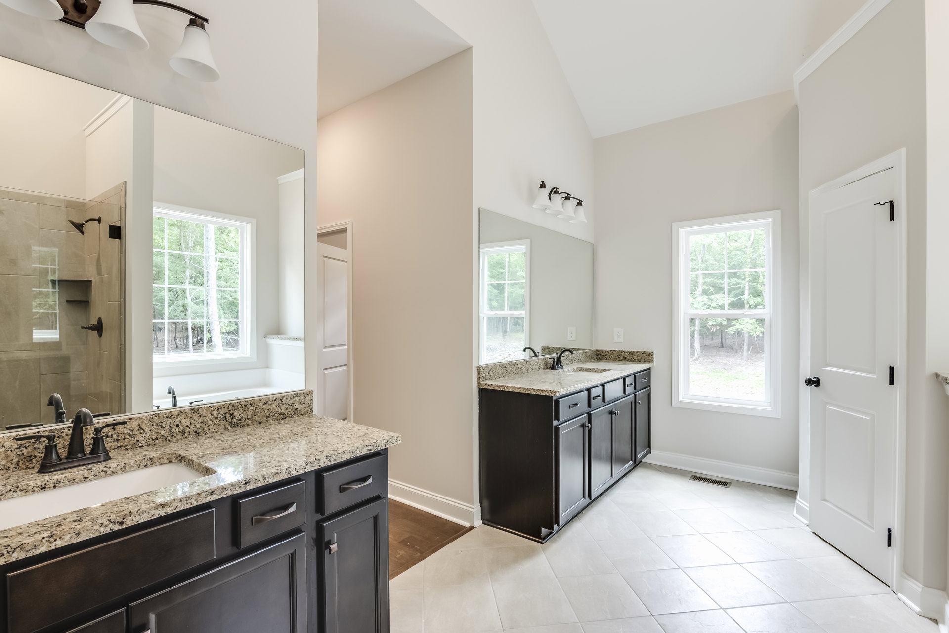 Bathroom with marble countertops, double sinks, white cabinetry, tile flooring, and a window overlooking trees.