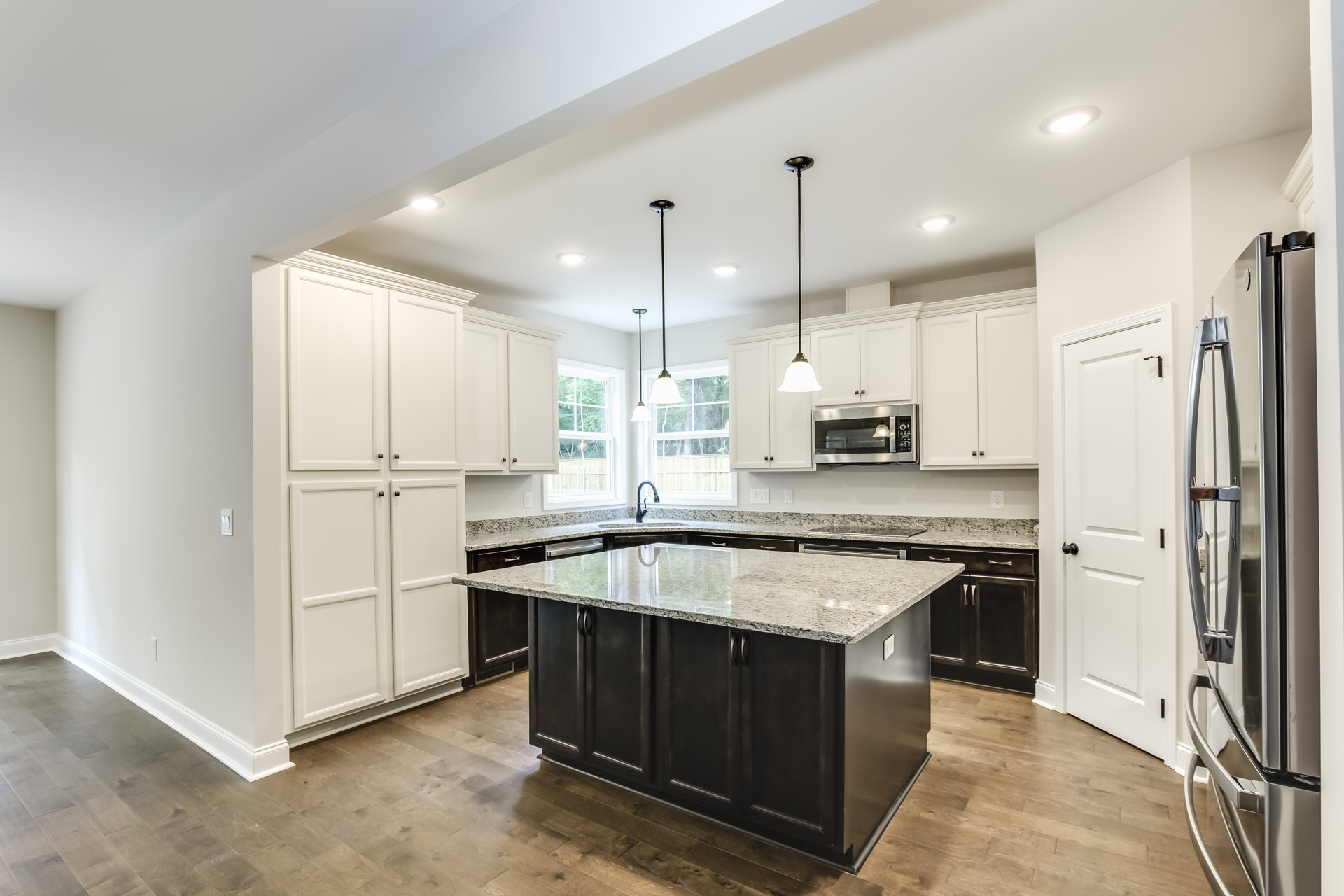 Spacious kitchen featuring a large granite island, white cabinetry, stainless steel microwave, tile flooring, modern light fixture with white shade, and close-up details of a white