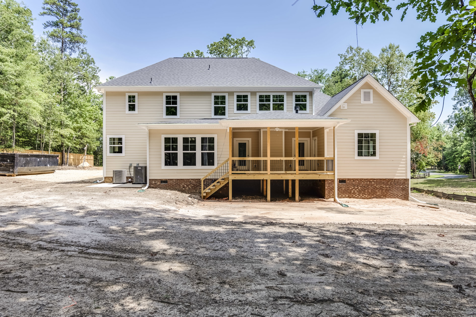 Two-story house with white siding, covered front porch with wooden posts, gravel driveway, white-trimmed windows, and mature trees in the yard