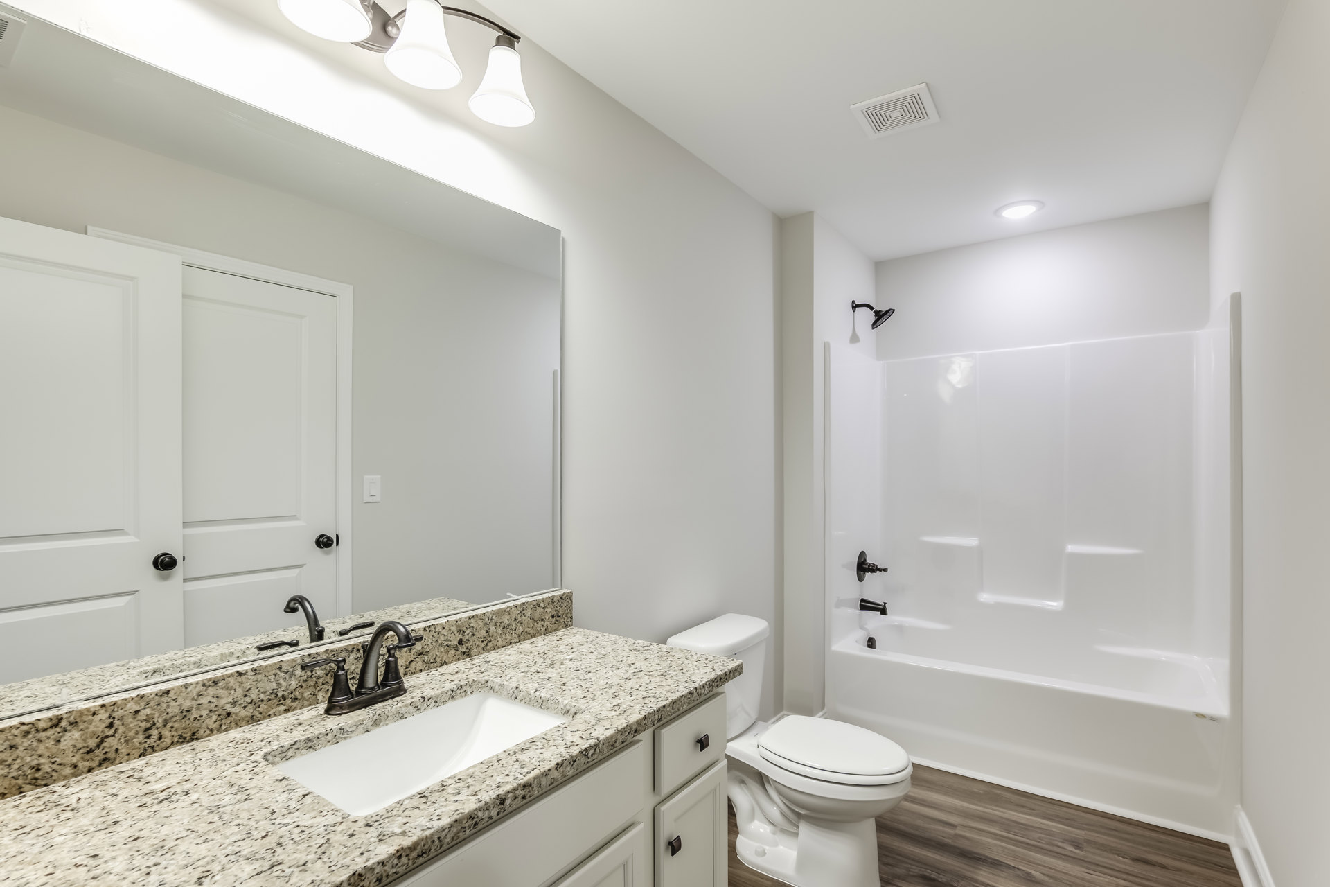 Marble countertop vanity with undermount sink, chrome faucet, glass-enclosed shower, white bathtub, and closed toilet in a tiled bathroom