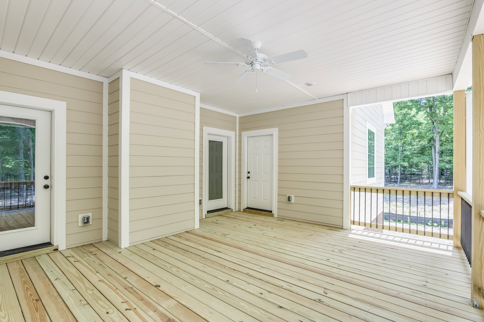 Bright room with wood flooring, white ceiling fan, white door with black hardware, glass panel door, and large window overlooking trees.