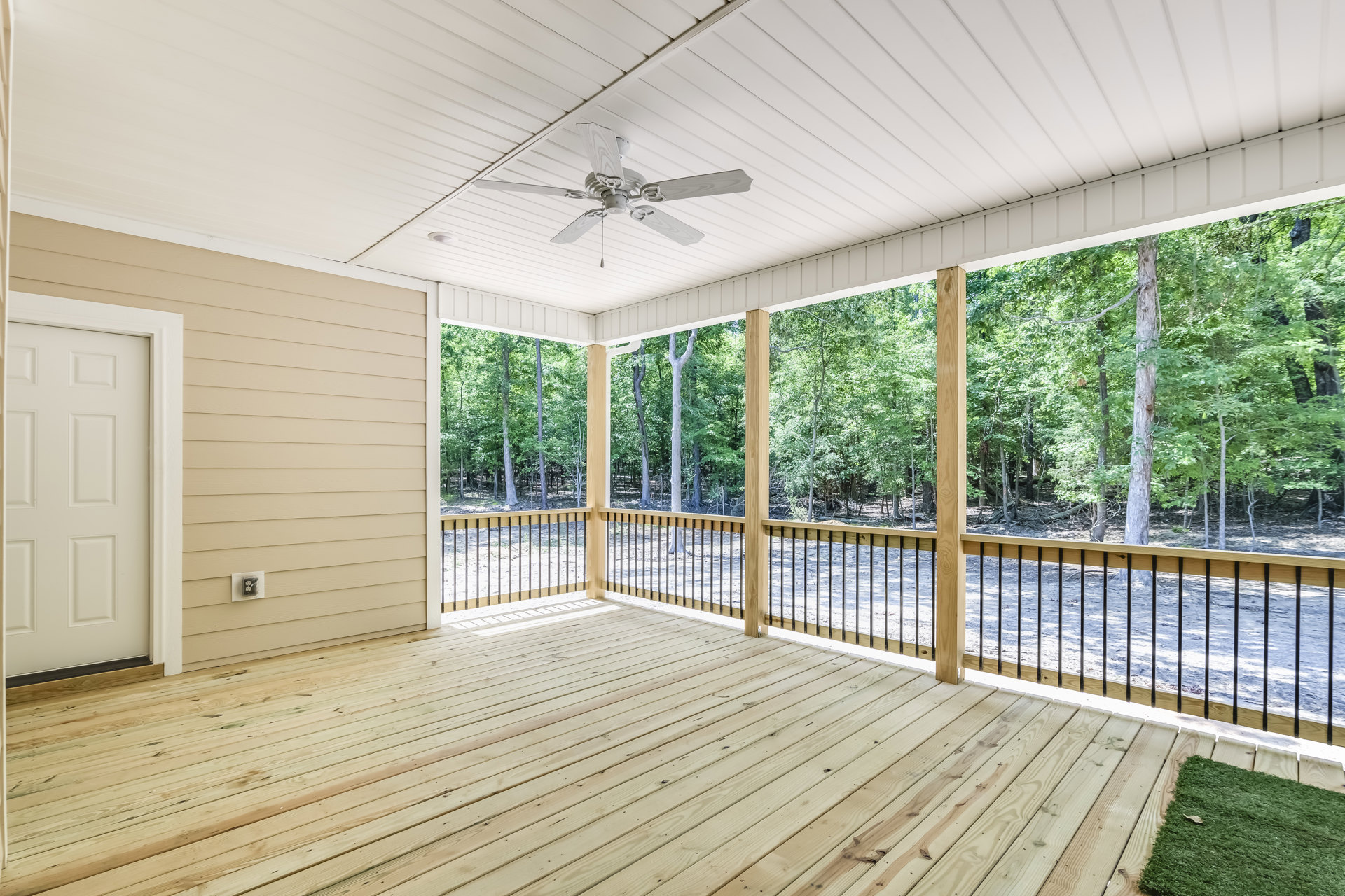 Wood-floored room with white ceiling fan featuring heart-shaped blades, white paneled door, and glass door opening to deck with railings; outdoor area visible with trees and grass