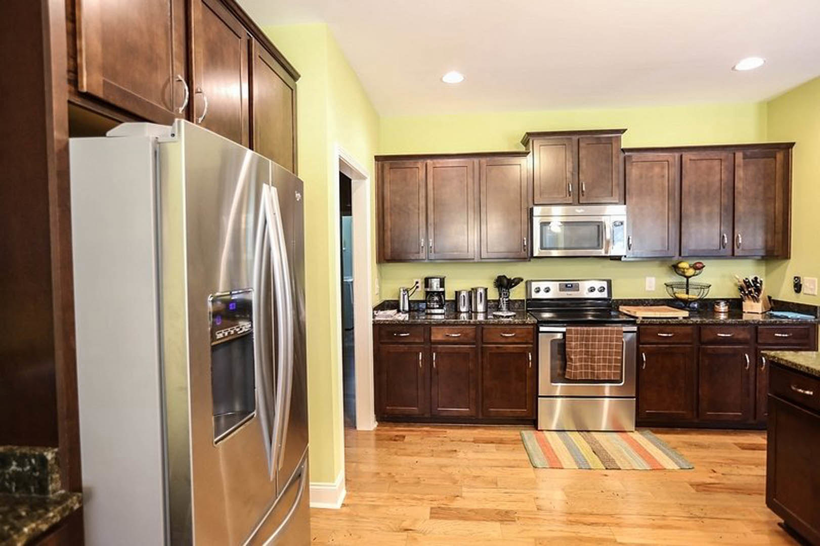 White kitchen with stainless steel refrigerator, built-in microwave, shaker cabinets, stone countertops, and a towel draped over stainless oven