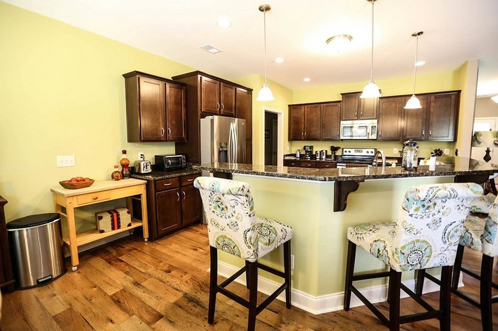 Open-concept kitchen featuring a marble-topped bar with wooden stools, stainless steel refrigerator, light wood cabinetry, and hardwood flooring