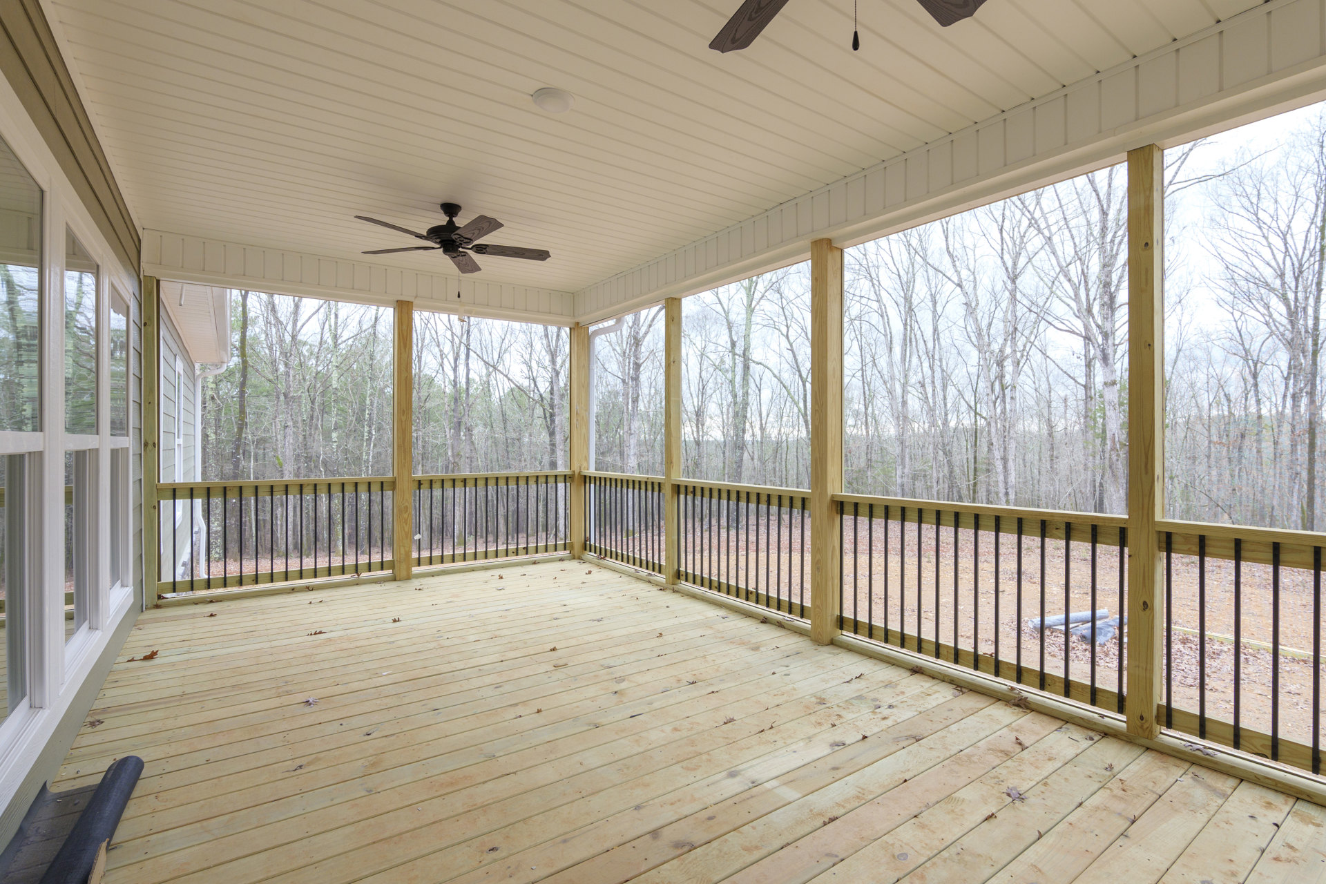 Wooden deck with metal railings, ceiling fan with wood blades, roll of black material on floor, roll of blue material on ground, small cracks visible in wood planks