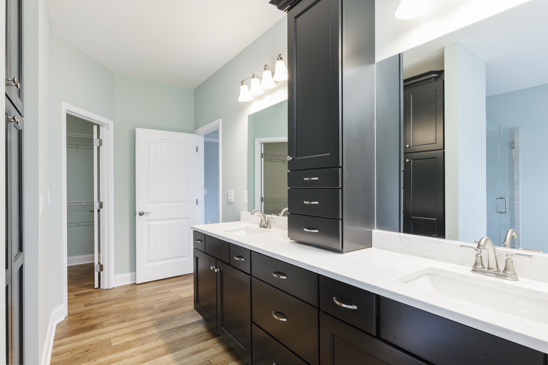 Bathroom featuring black cabinetry with silver knobs, white quartz countertops, undermount sink, chrome faucet, white tile backsplash, and a white door with a silver handle.