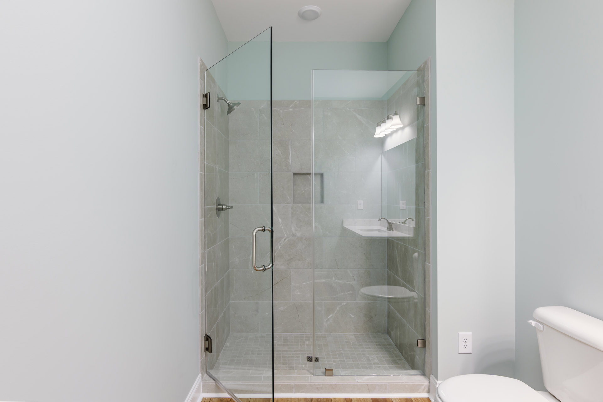 Bathroom with glass shower enclosure, white toilet, tiled walls, chrome shower knob, and modern sink.