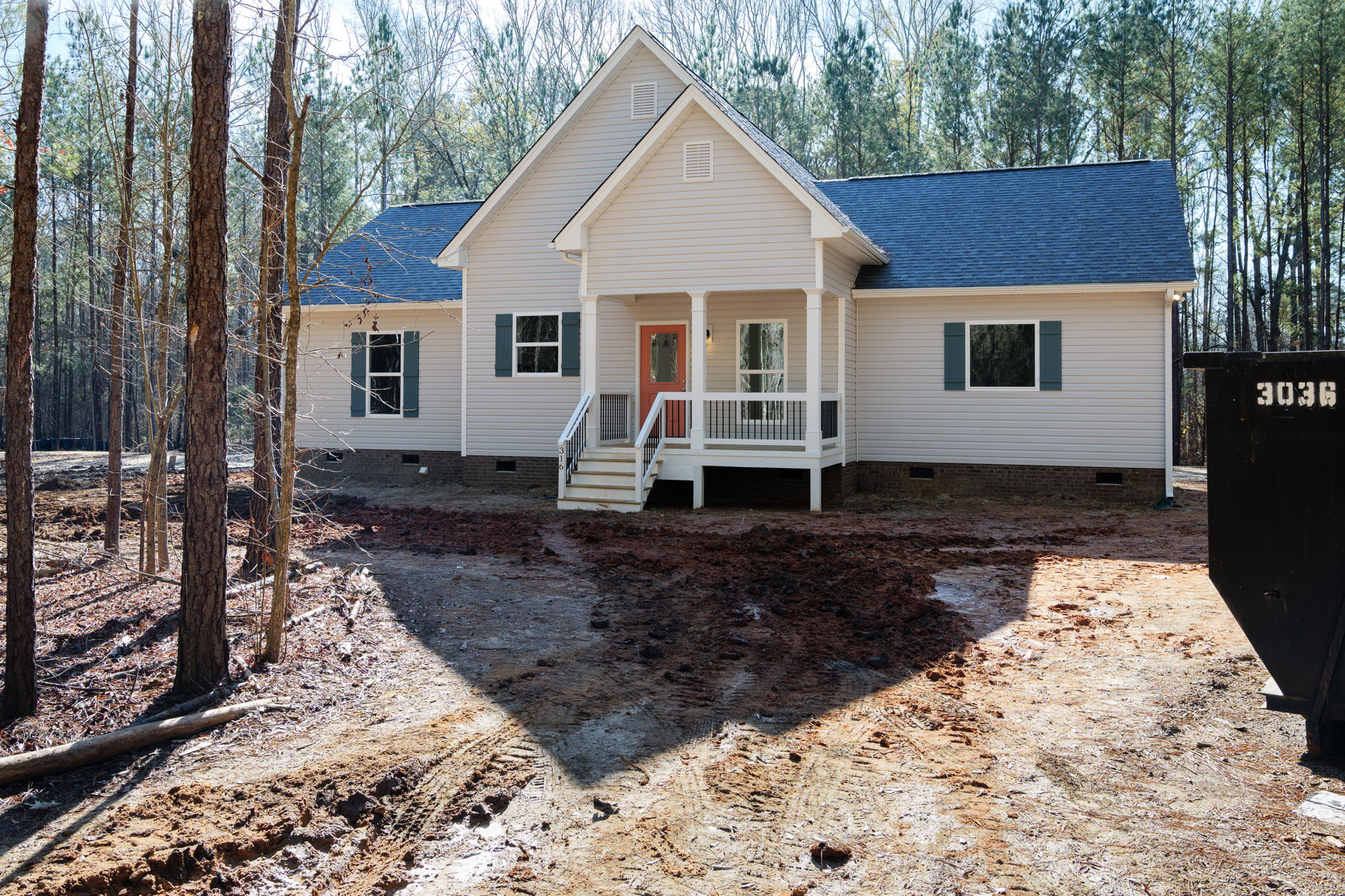 White siding house with black railing porch, red front door, driveway, white-framed windows, tree branches in background
