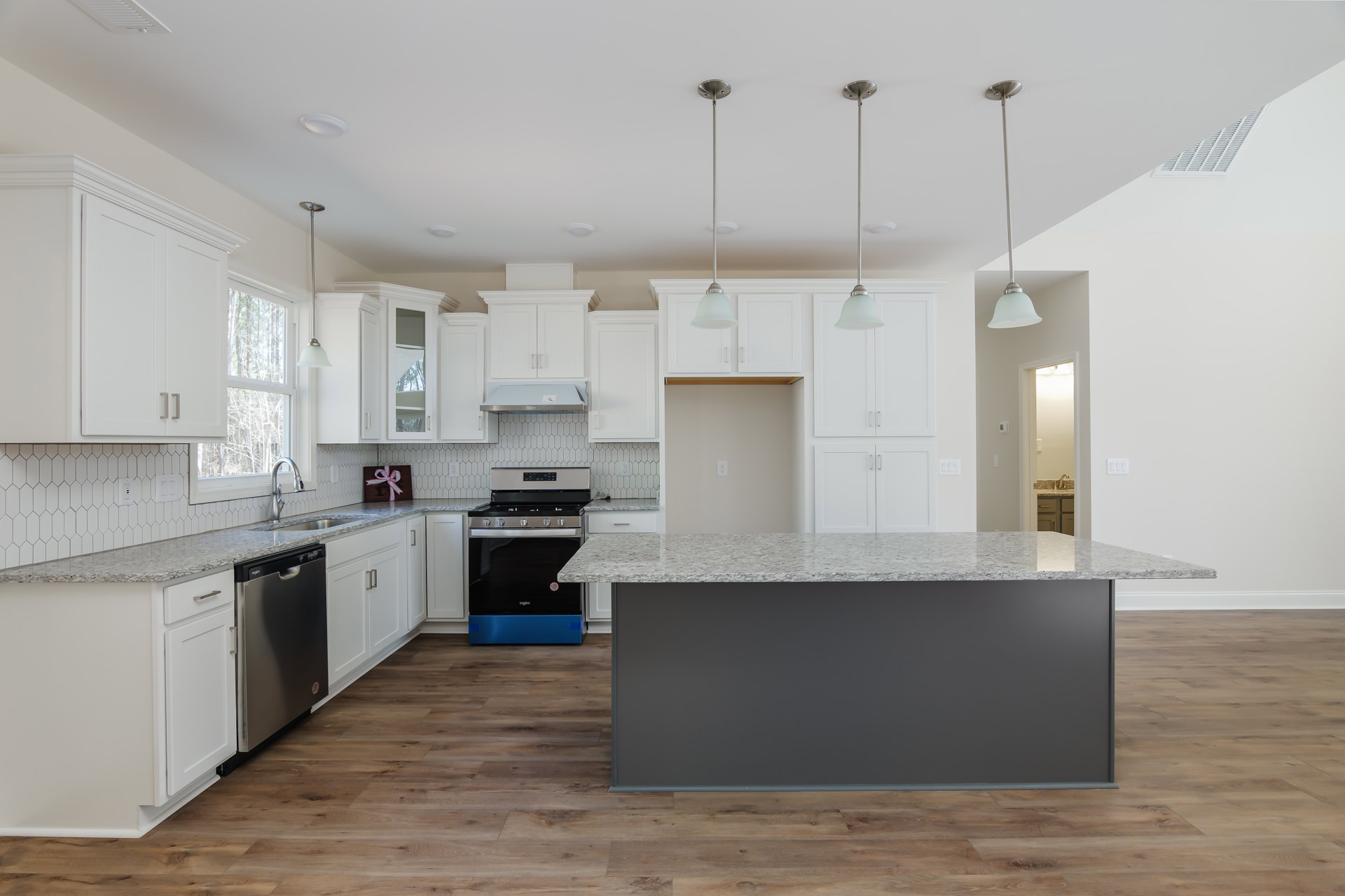 Spacious kitchen featuring a large central island with contrasting black and white countertops, modern cabinetry, stainless steel stove with black and blue handle, pendant