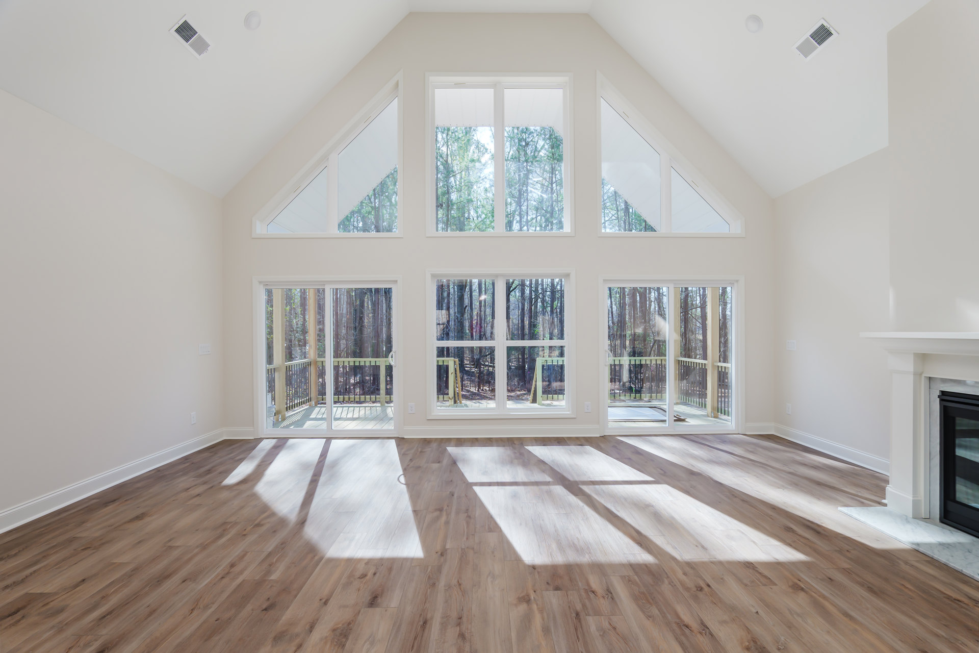 Sunlit room with hardwood floors, white-framed windows, wall vent, and molding, opening onto a deck.