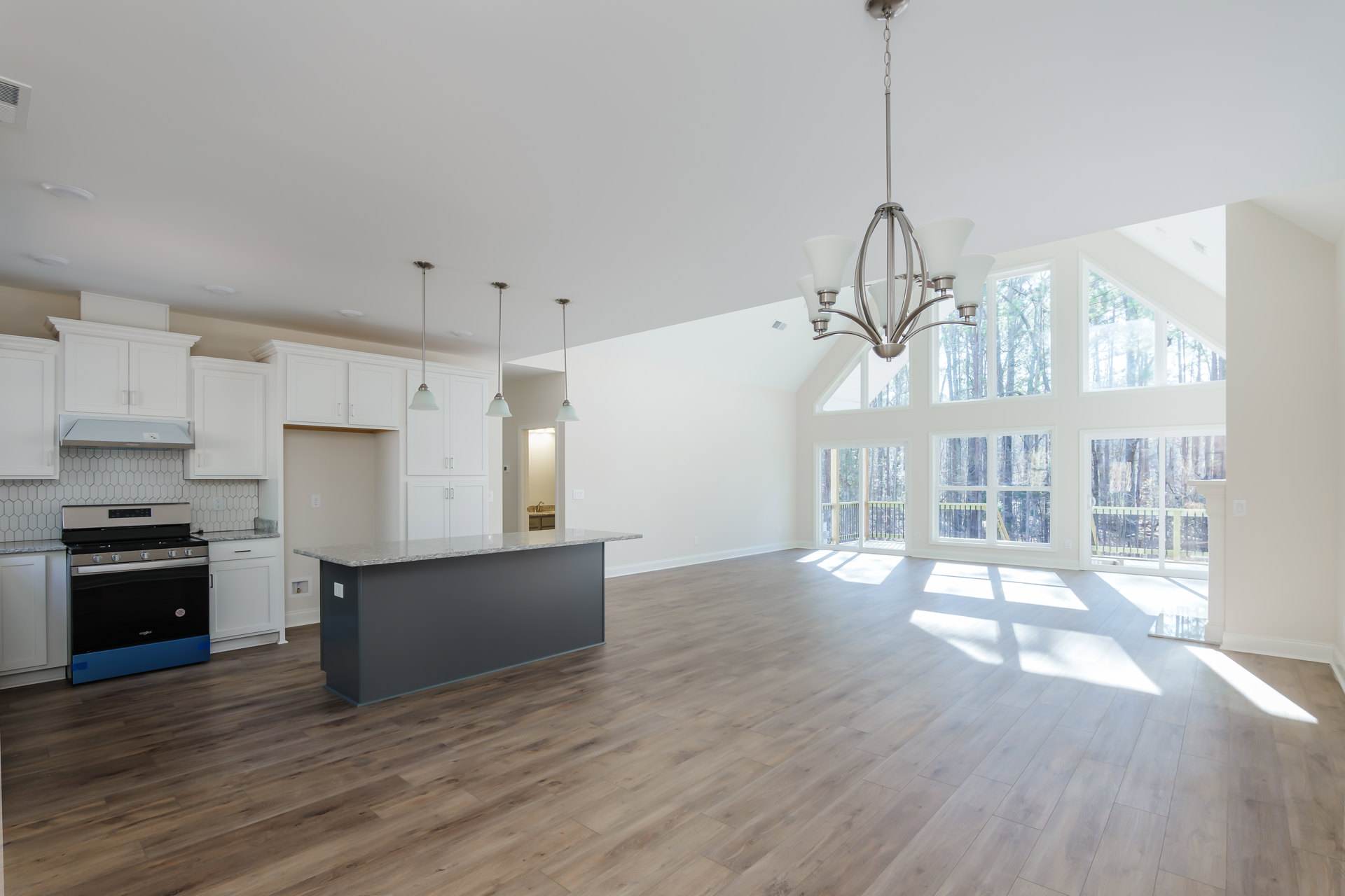 Spacious kitchen with wood flooring, central island featuring grey countertop, black and blue stove, modern cabinetry, and contemporary light fixture