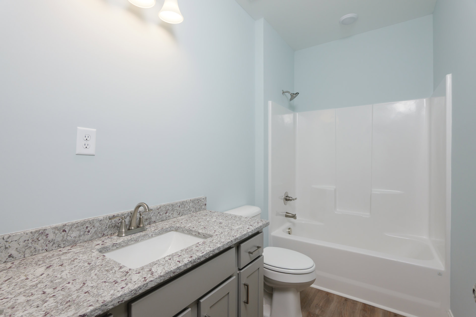 Modern bathroom with white tile walls, built-in shower, white sink and cabinet, closed toilet, quartz countertop, salt and pepper shakers, electrical outlet, and smooth white
