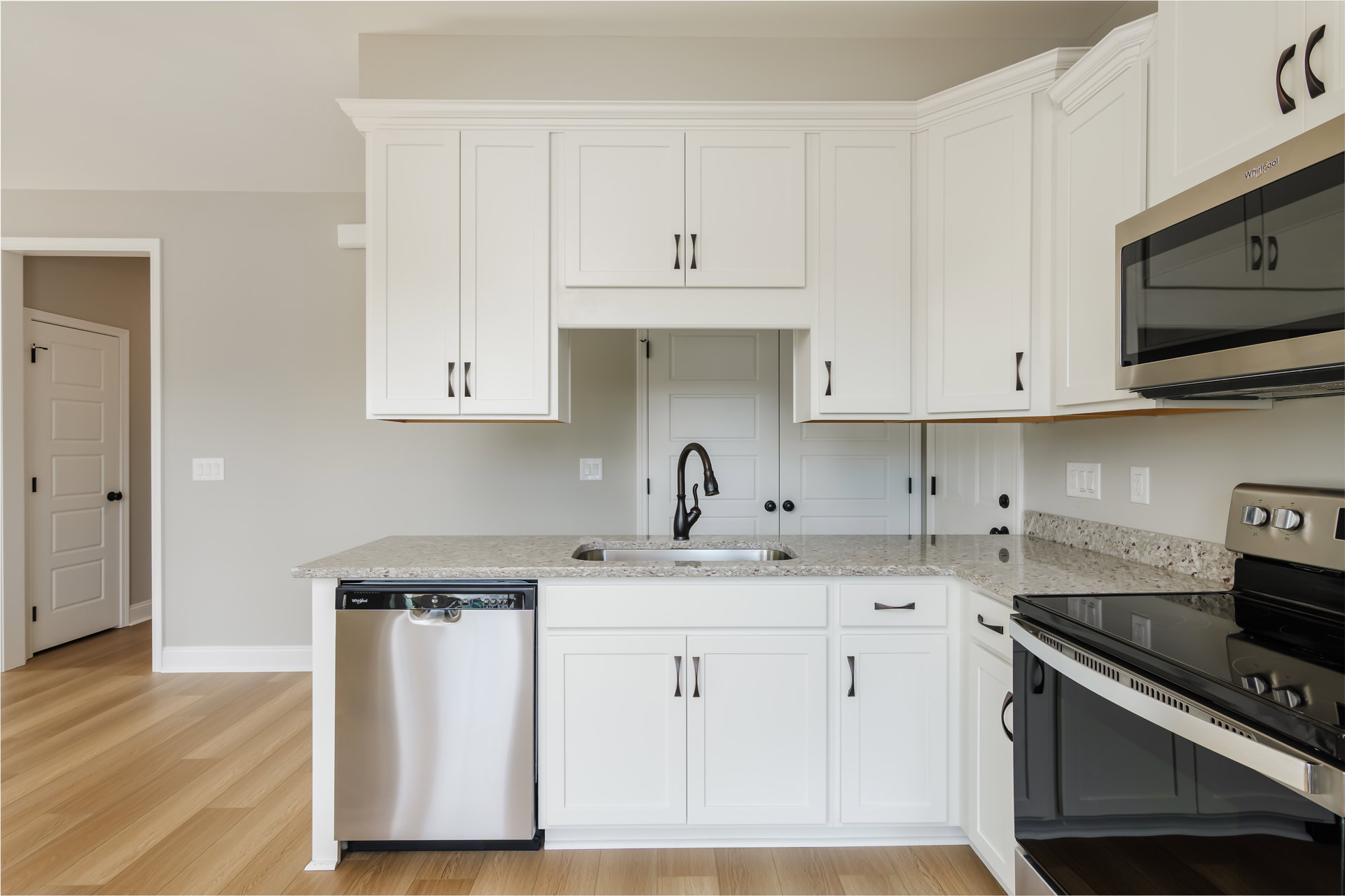 White kitchen cabinets with black appliances, including a stove, microwave, and dishwasher; silver faucet over a sink; white door with black knob; light countertops and neutral