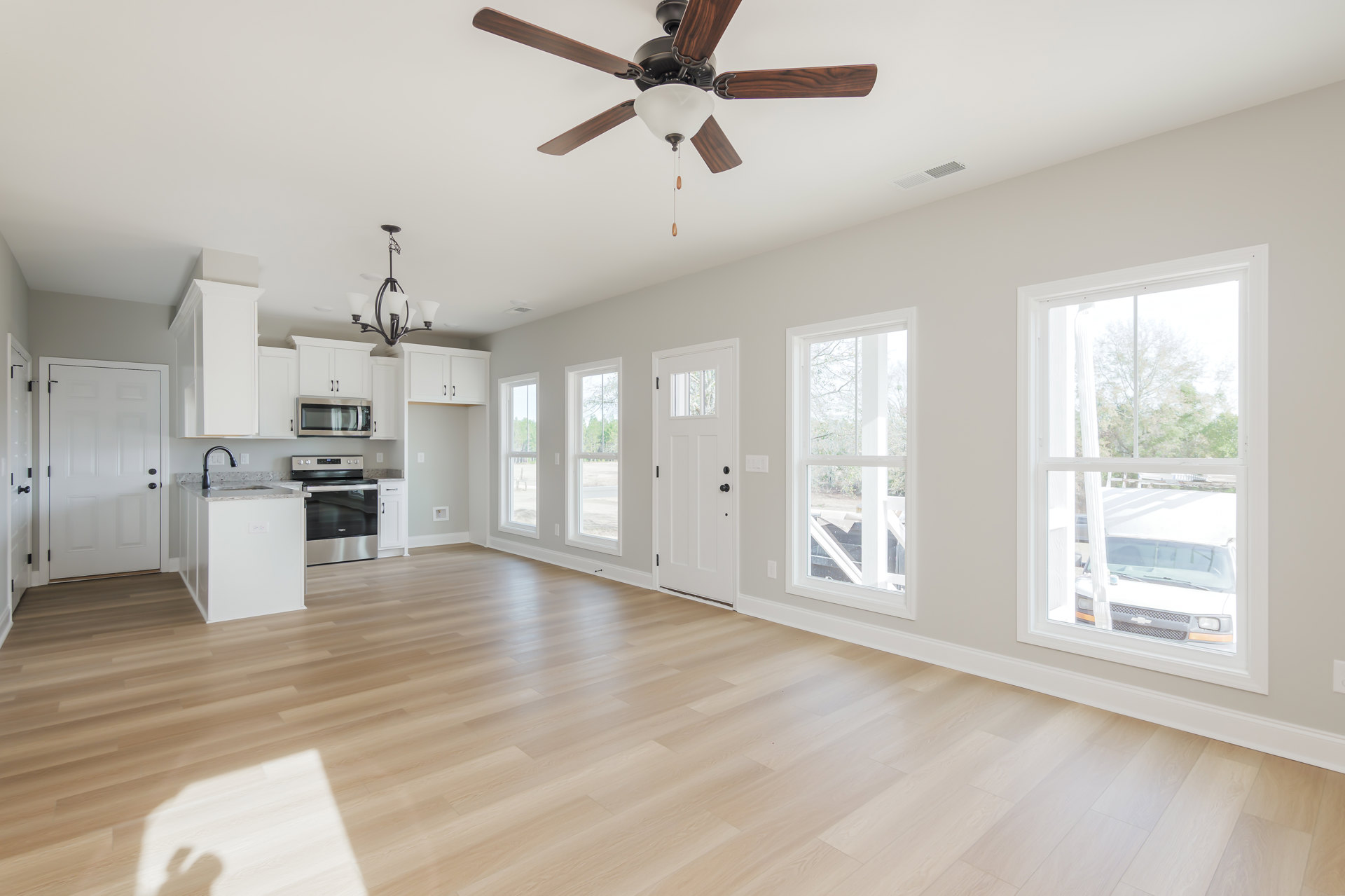 Ceiling fan with light fixture, hardwood floor, white door with black knobs, black faucet on marble countertop, windows letting in natural light