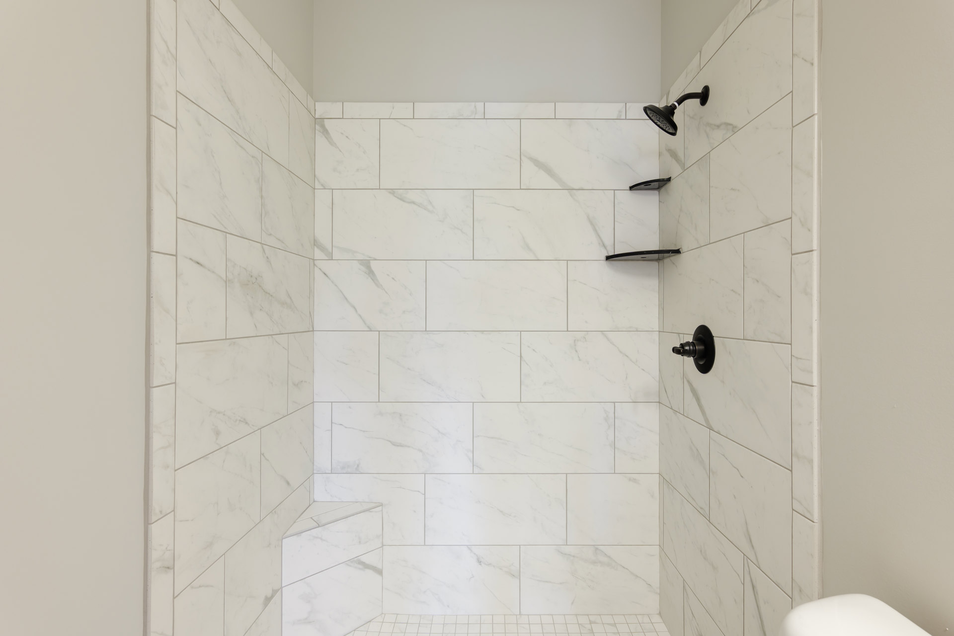 Walk-in shower featuring patterned tile floor, matte black shower head and fixtures, white tiled walls, and minimalist plumbing accessories