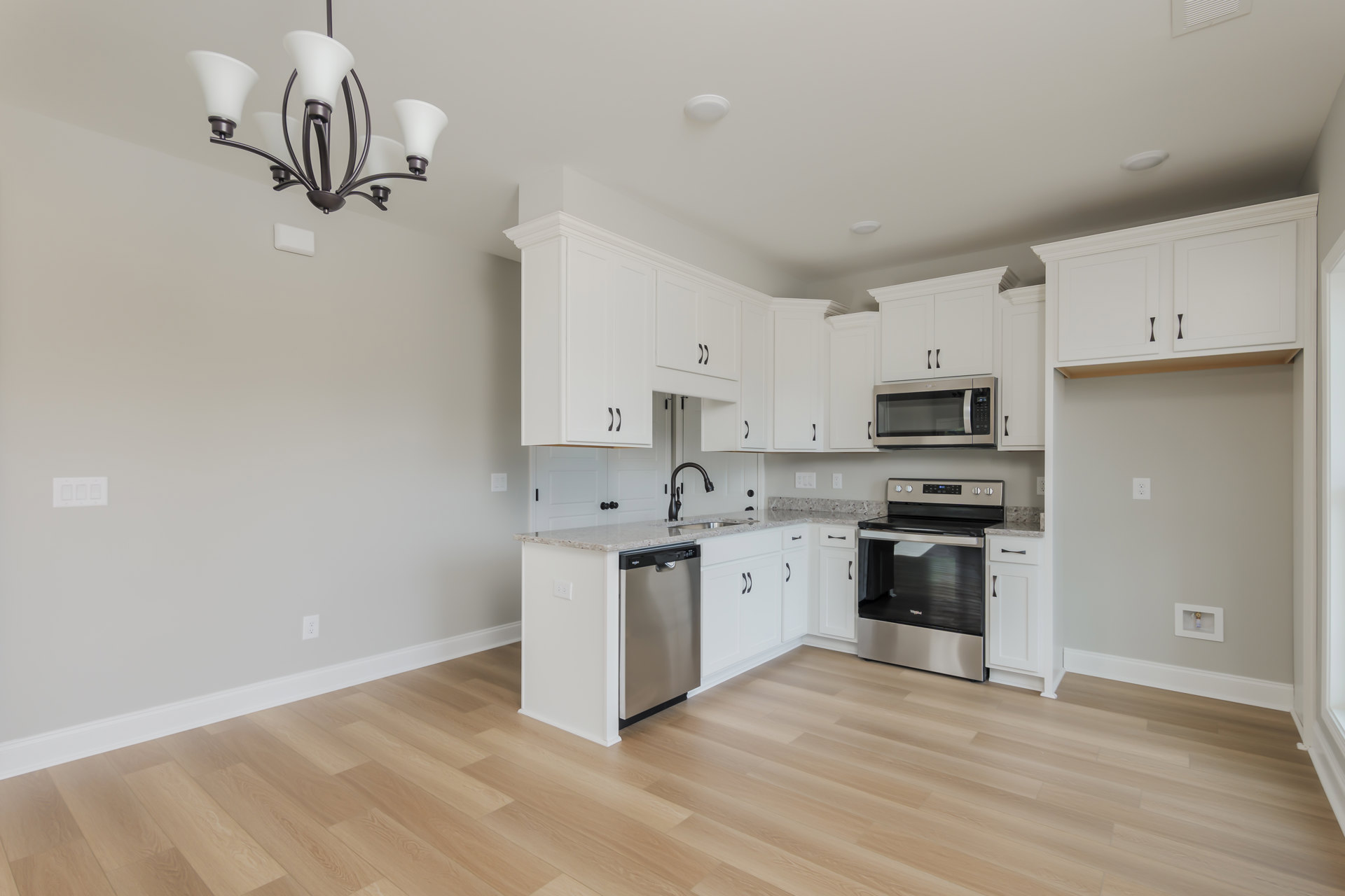 White shaker cabinets, stainless steel appliances including a glass-door stove and refrigerator, wood plank flooring, quartz countertops, modern chandelier, and built-in microwave.