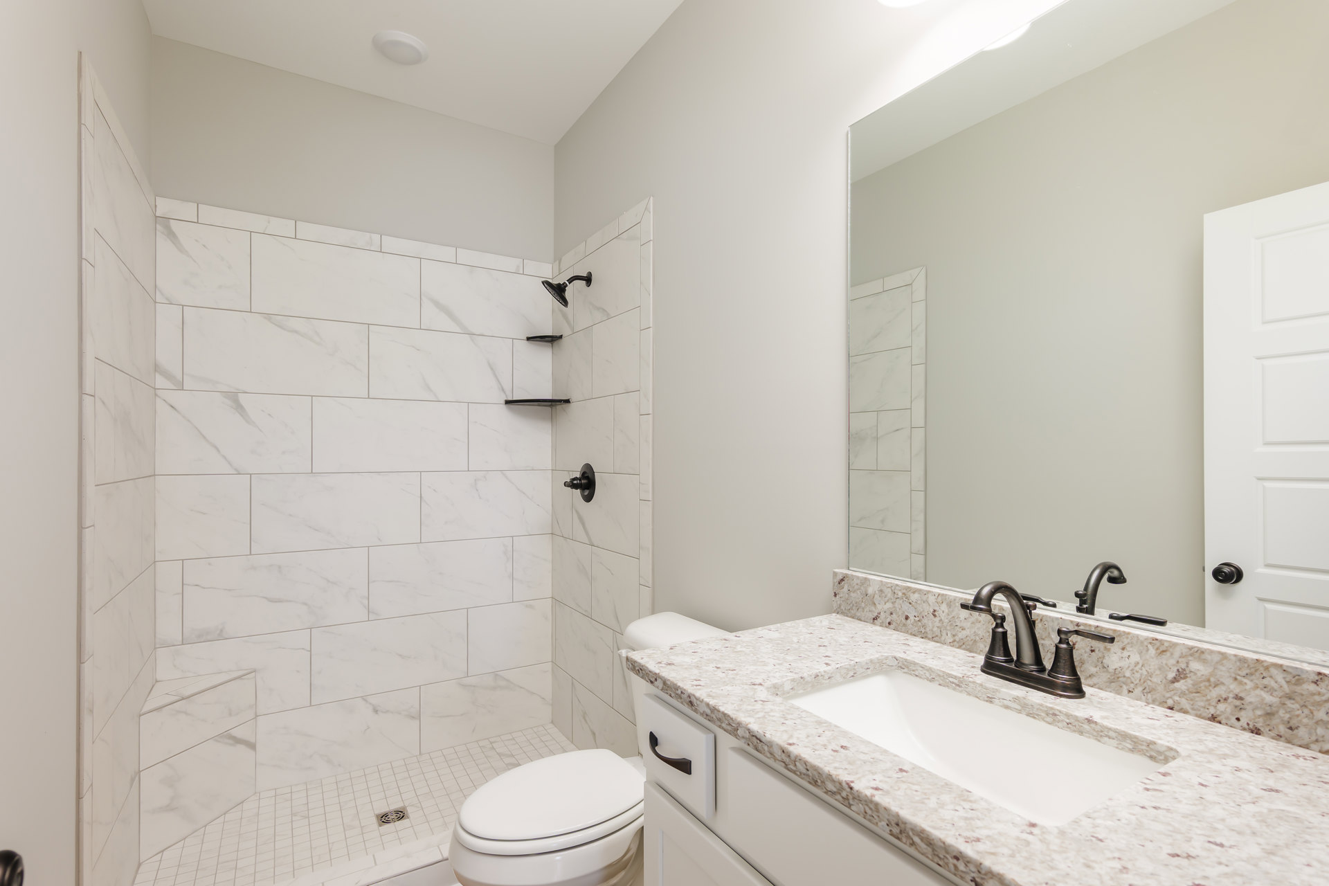 Modern bathroom featuring a white porcelain sink with chrome faucet, rectangular mirror above, glass-enclosed shower with gray tile walls, and a white toilet with closed lid.