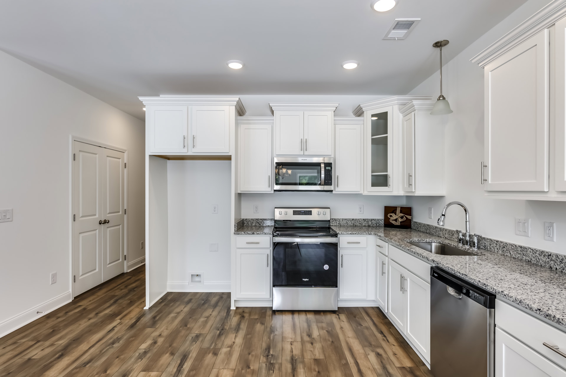 White kitchen cabinets and granite countertops with a black and silver oven, built-in microwave under a light fixture, dishwasher beside marble counter, brown gift box with bow on
