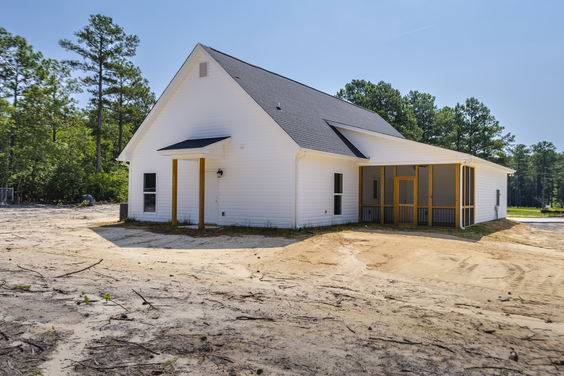 White siding house with covered front porch, screen door, dirt yard, and white outbuilding in the background
