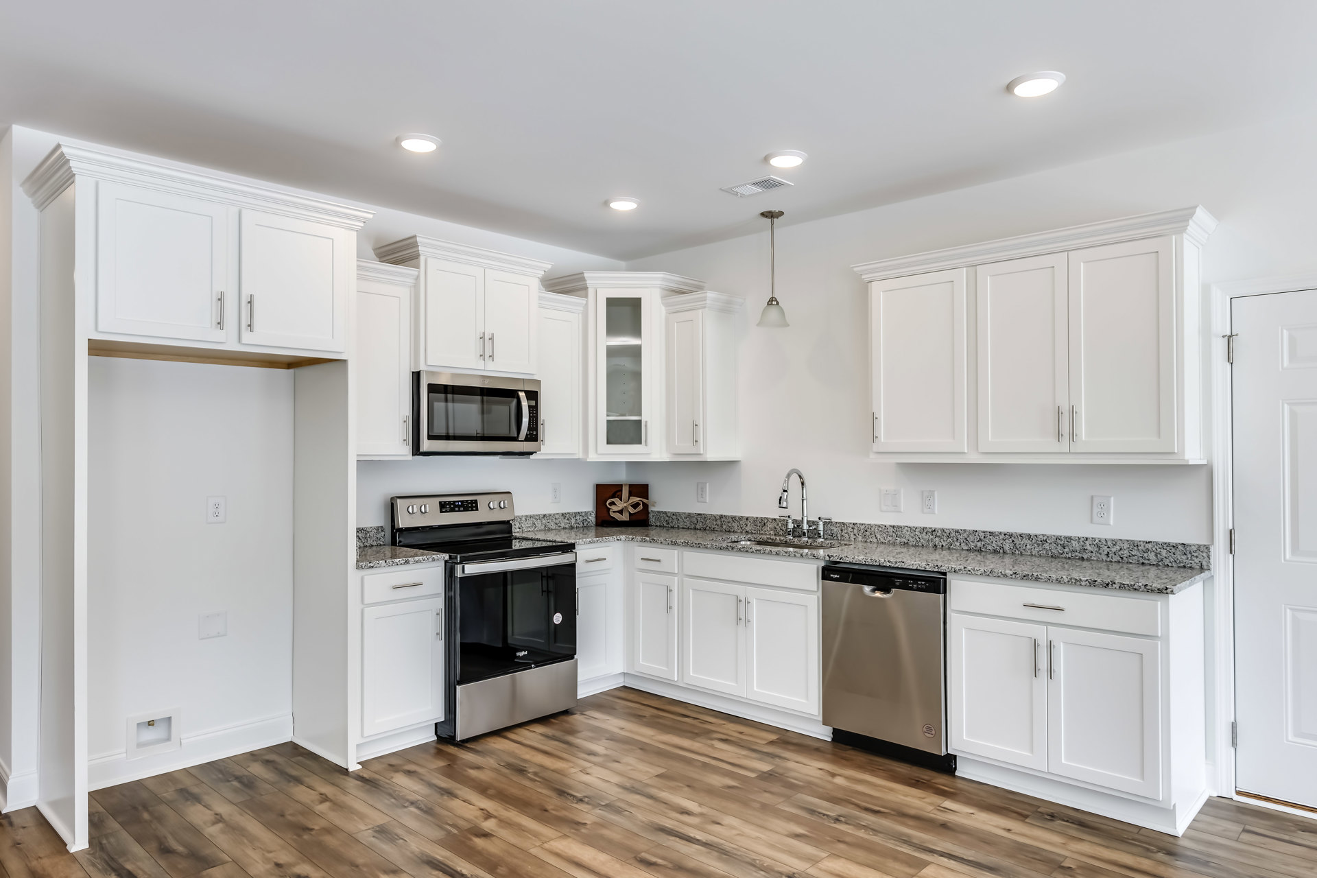 White kitchen cabinets with black handles, granite countertops, stainless steel microwave, stove, and dishwasher, brown gift box with white ribbon on counter, light-colored