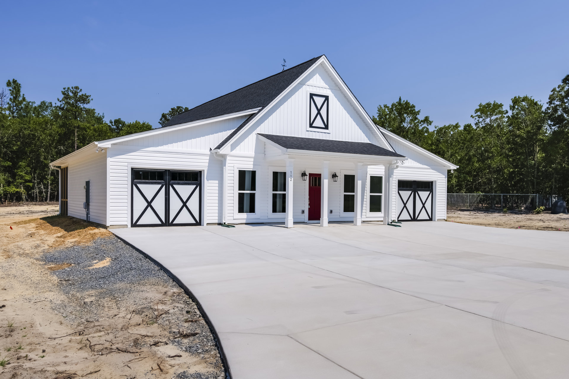 White two-story house with white pillars, red front door, double garage doors, paved driveway, and landscaped front yard with trees.