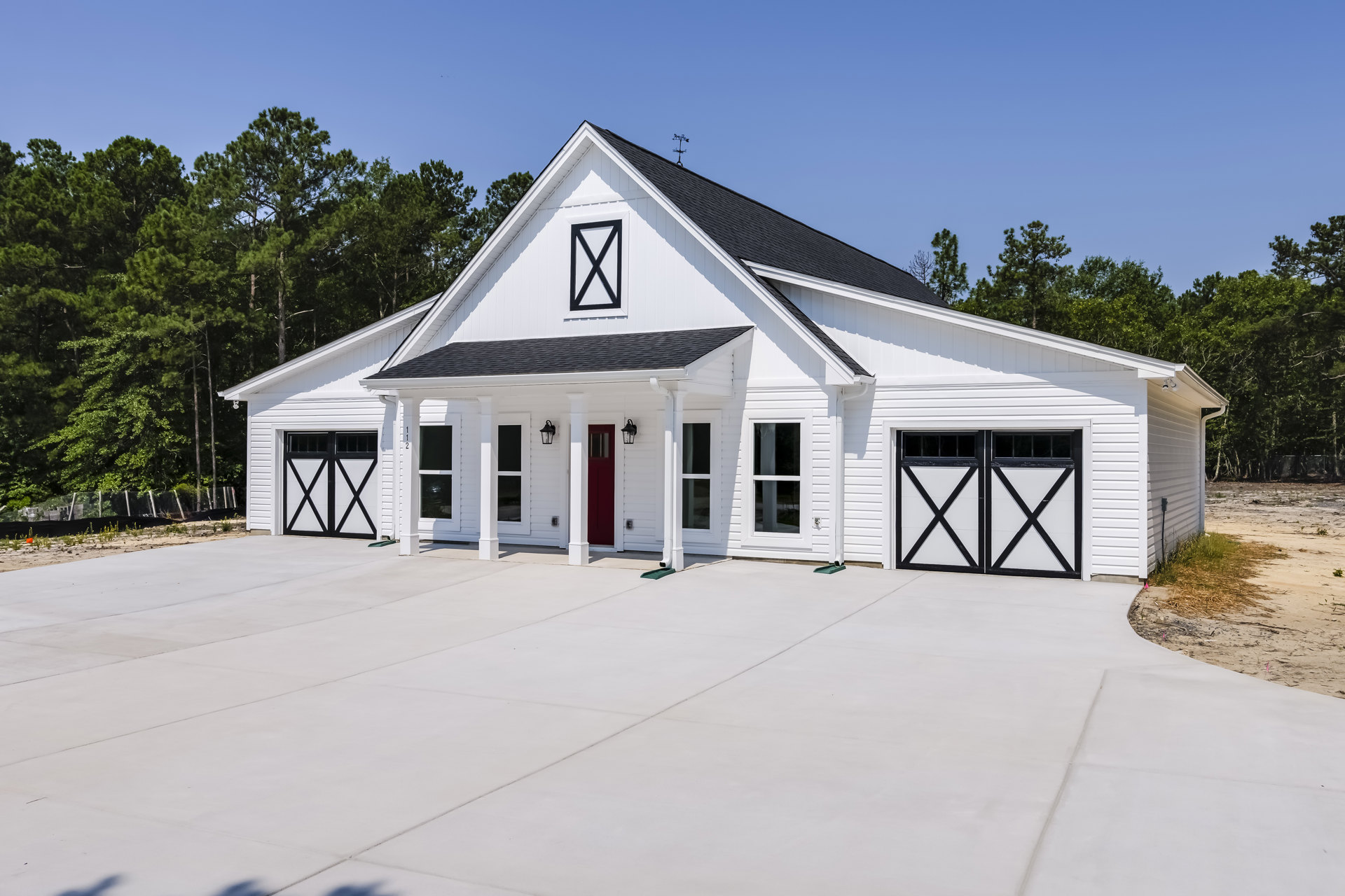 White two-story house with attached garages, white siding, black garage door accents, white columns, red front doors, and manicured landscaping.