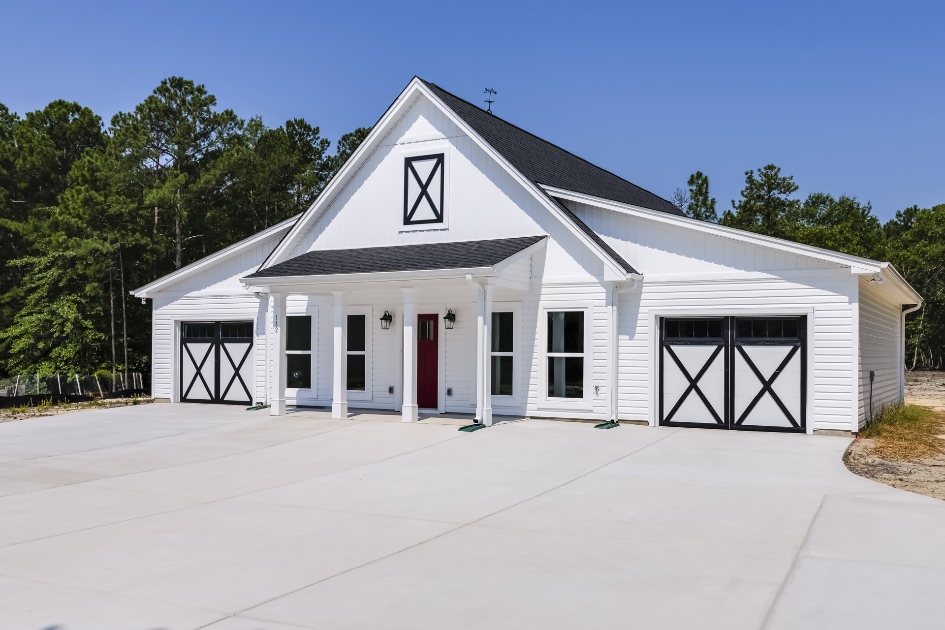 White two-story house with black-trimmed windows, attached garage featuring white doors, black and white address sign, paved driveway, and landscaped front yard with trees.