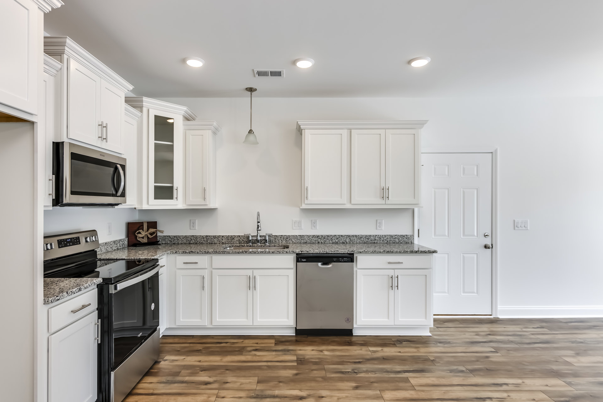White kitchen cabinets with silver handles, black appliances including a microwave and dishwasher, marble countertop, and a brown gift box with a bow on the counter.