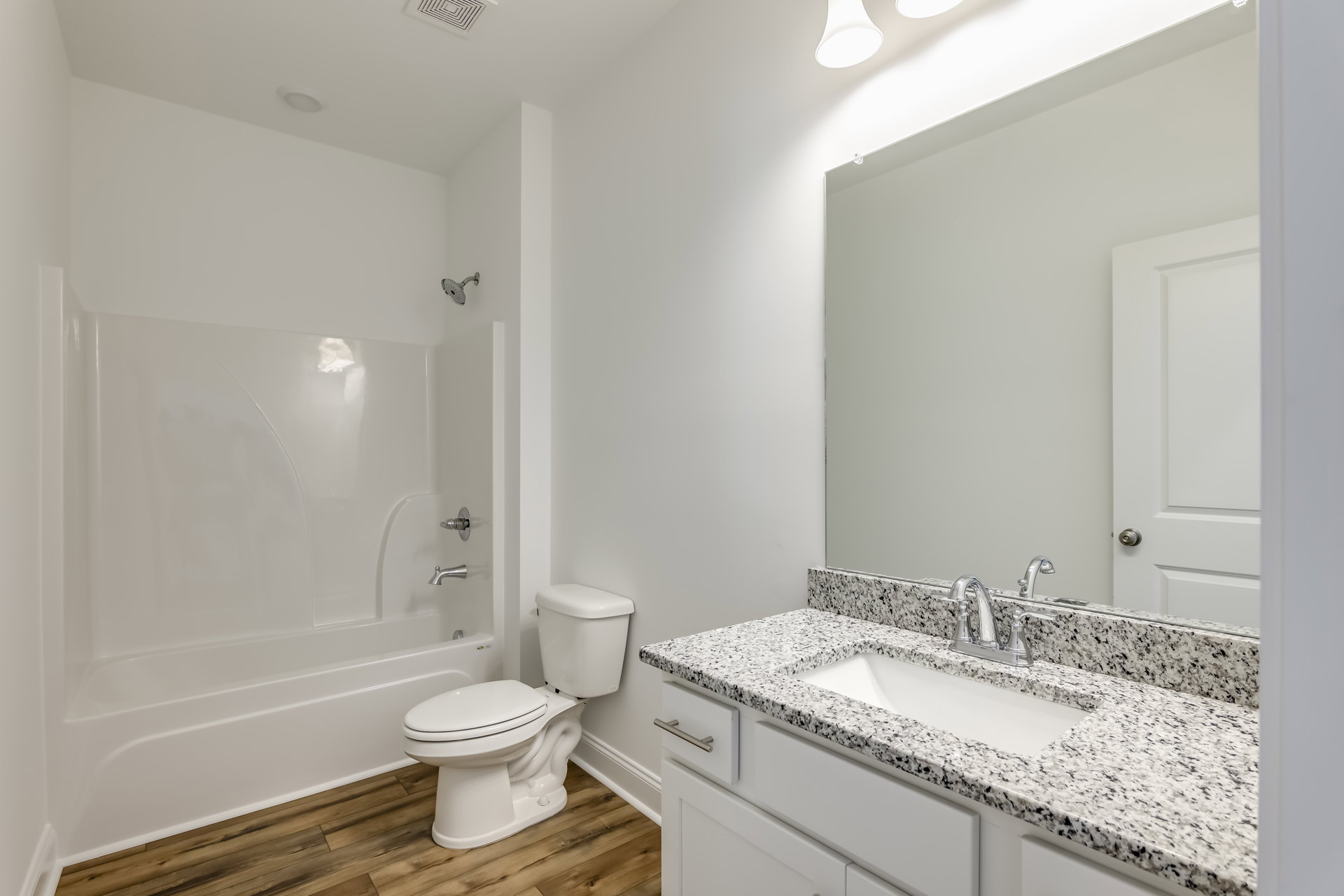 Marble countertop with undermount sink and chrome faucet, white toilet with closed lid, white bathtub, light tile flooring, neutral wall color