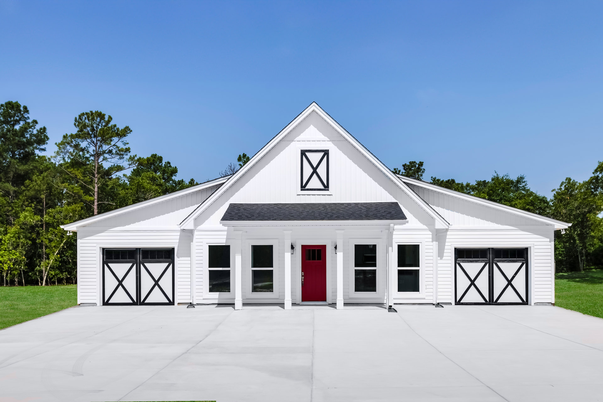 White siding exterior with black-framed windows, red front door featuring a lock, attached garage with white door, black and white address sign, landscaped front yard with trees