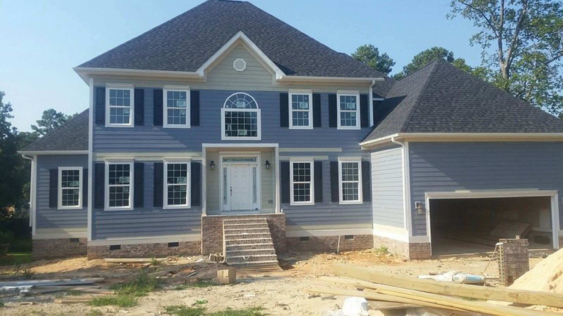 Two-story house under construction with blue roof, white siding, white door, white-framed window, and partially built exterior staircase