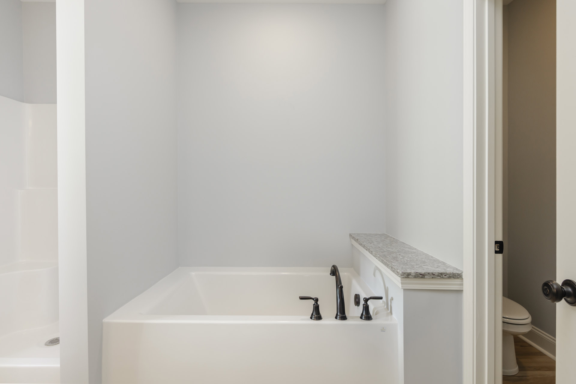 Freestanding white bathtub with chrome faucet, closed toilet, white tile walls, and minimalist countertop in bright bathroom