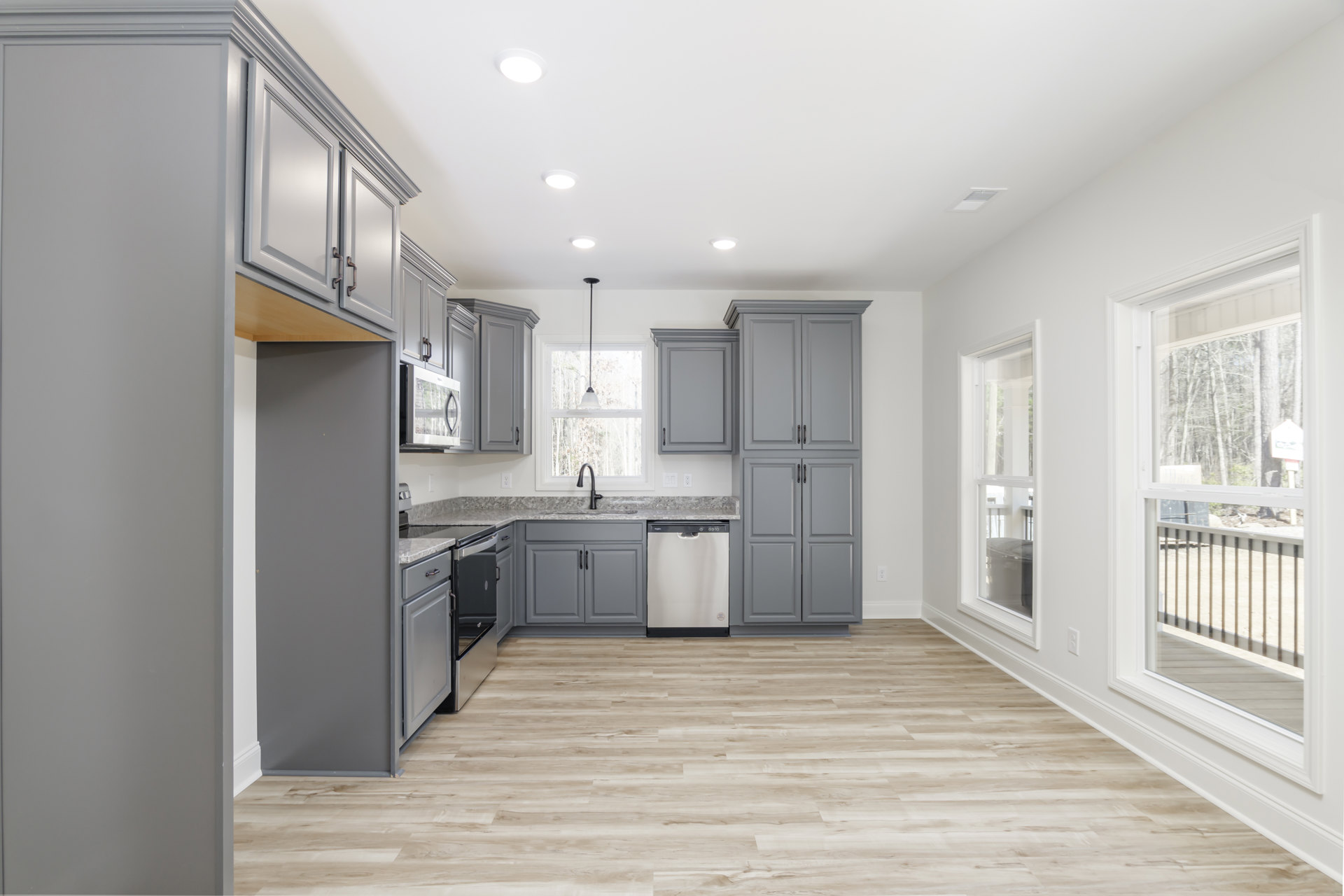Grey shaker cabinets with black handles, white quartz countertop, stainless steel dishwasher, hardwood flooring, and a deep stainless sink in a modern kitchen.