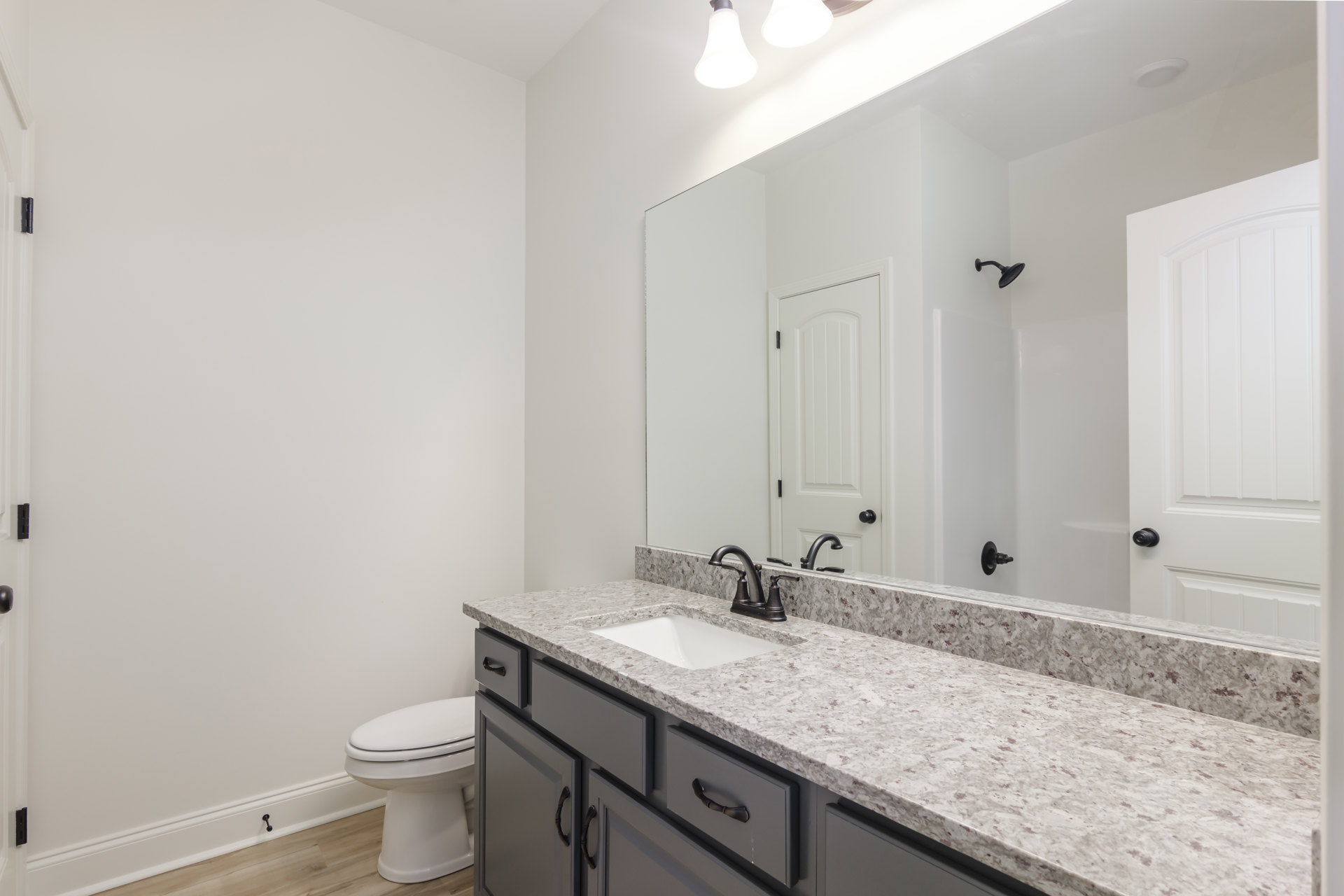 Modern bathroom with white ceramic sink, chrome faucet, rectangular mirror above vanity, white toilet, light bulb fixture, and tiled walls