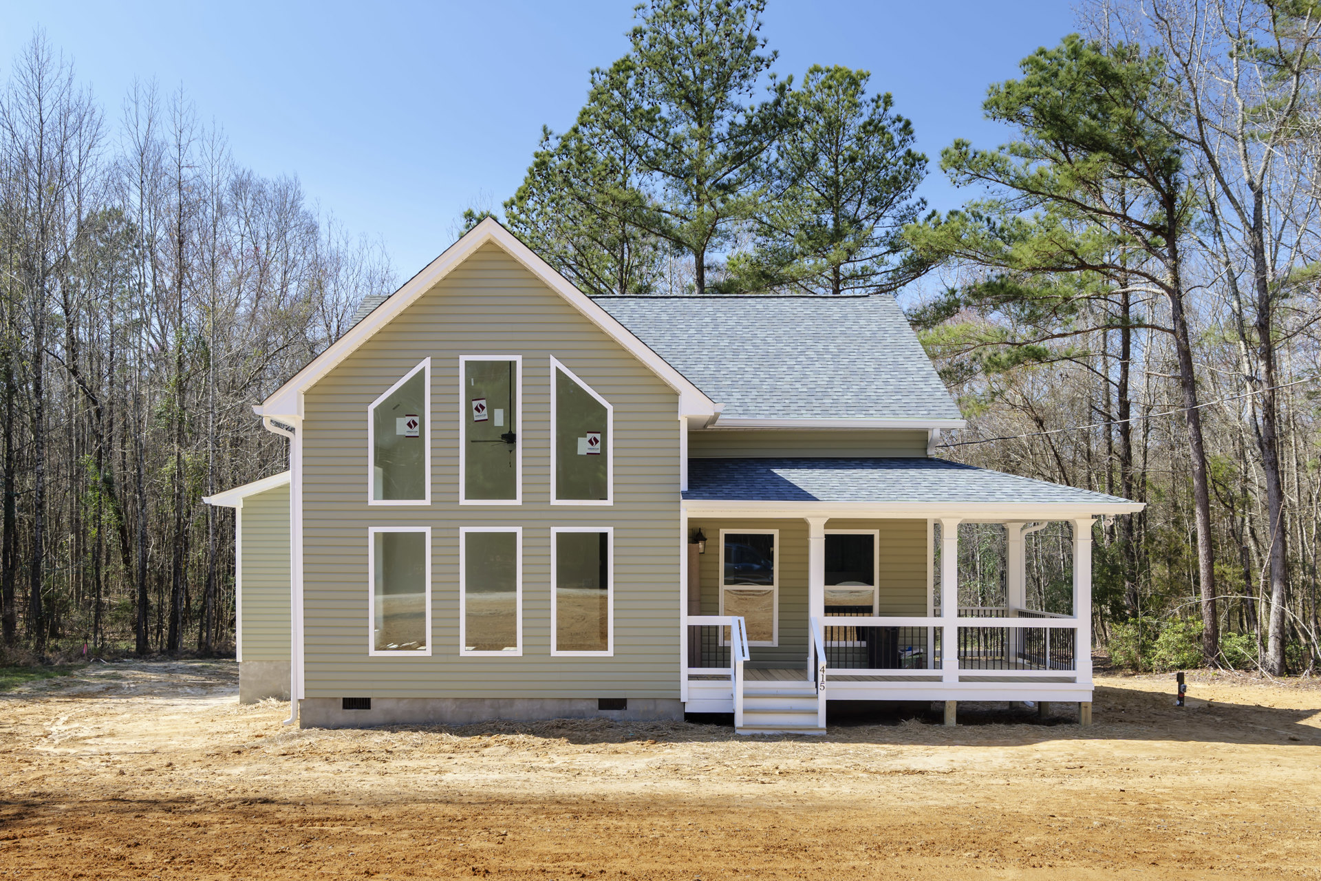 White siding house with two porches, black metal railings, multiple windows with white frames, tree in front yard, blue sky overhead