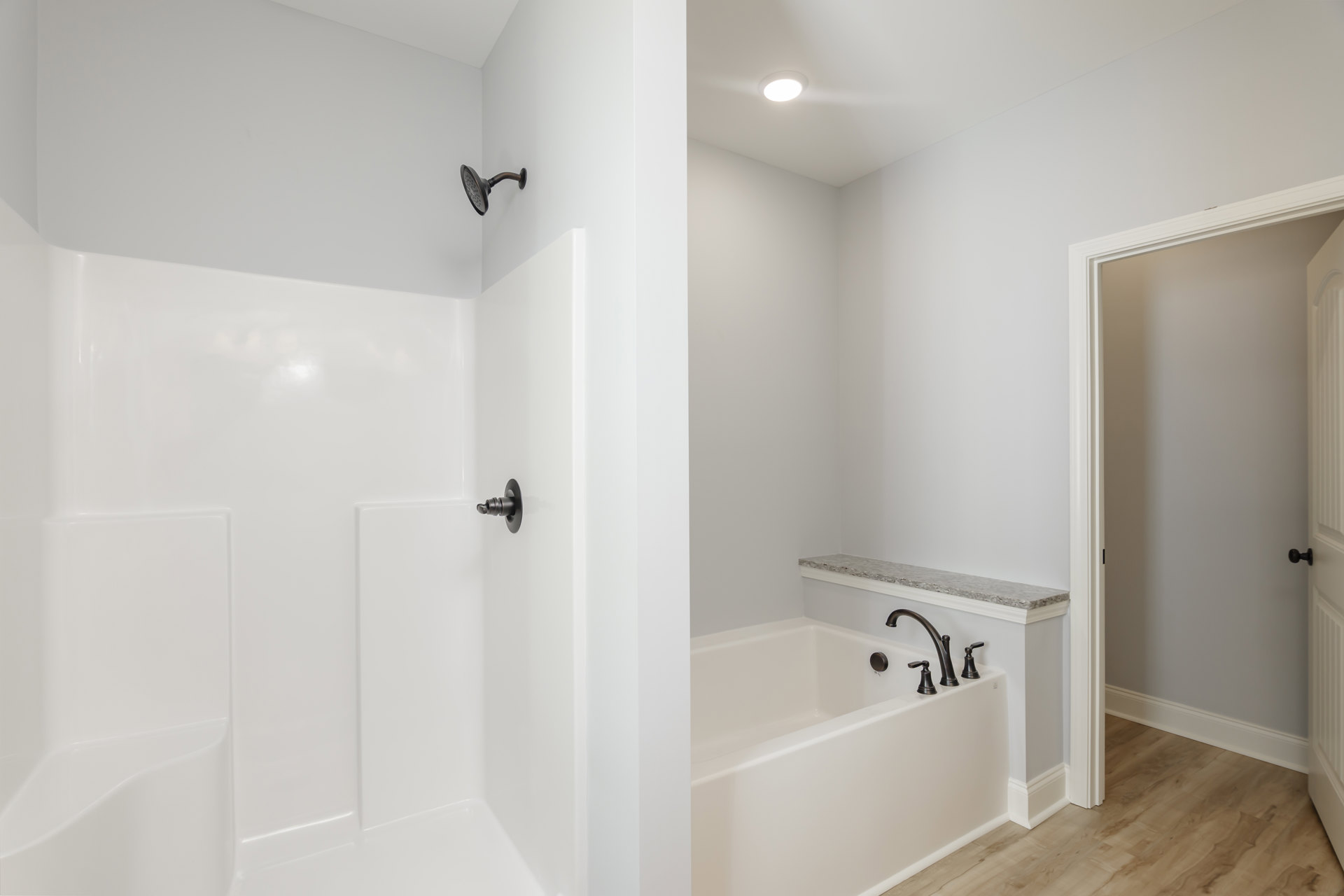 Bathroom featuring a white bathtub and glass-enclosed shower, ceiling light, metal shower head, open door to adjacent room, close-up of chrome faucet, white countertop with