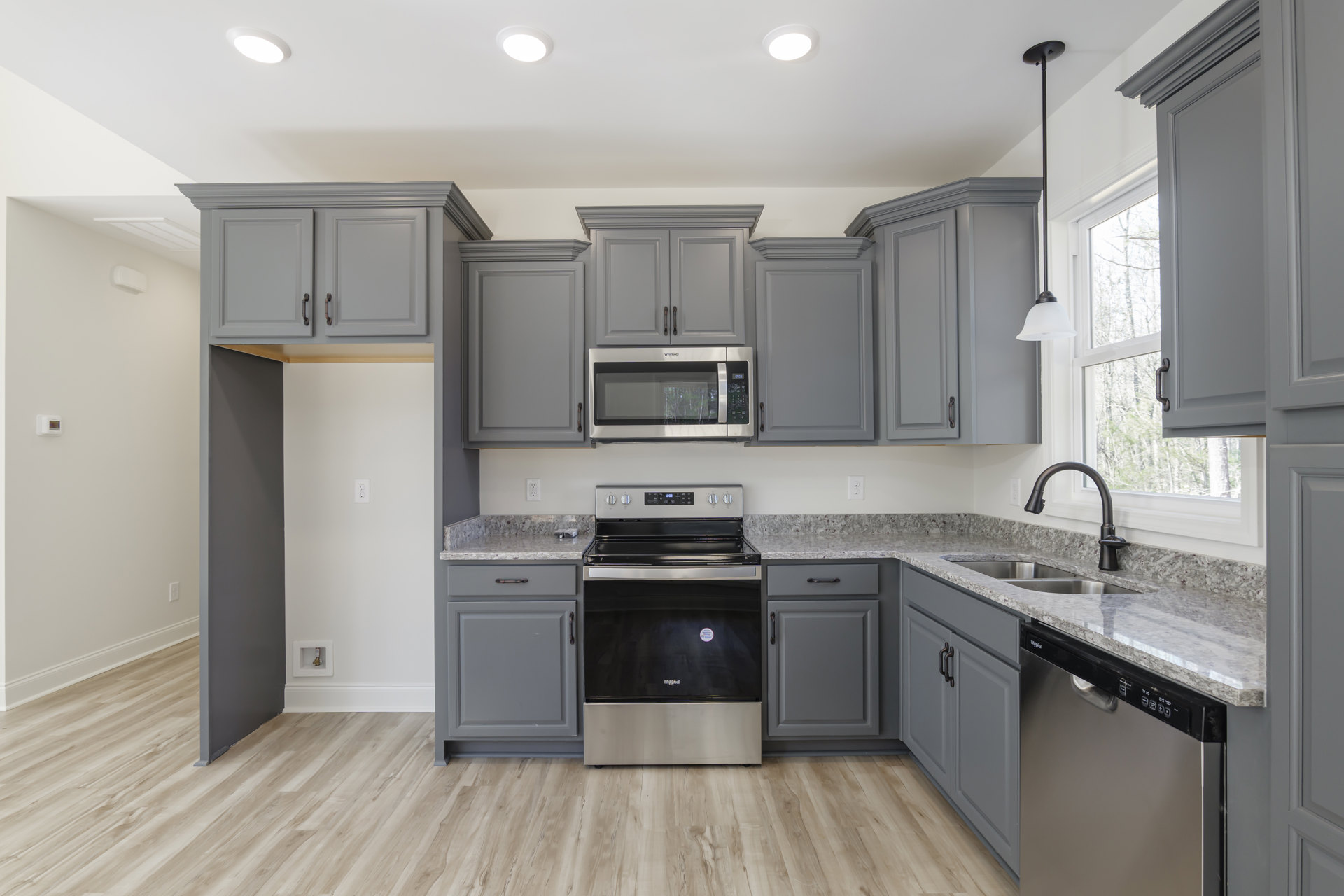 Grey kitchen cabinets with granite countertops, black and silver stove, stainless steel microwave, dishwasher beneath marble counter, white door with black handle, light-colored